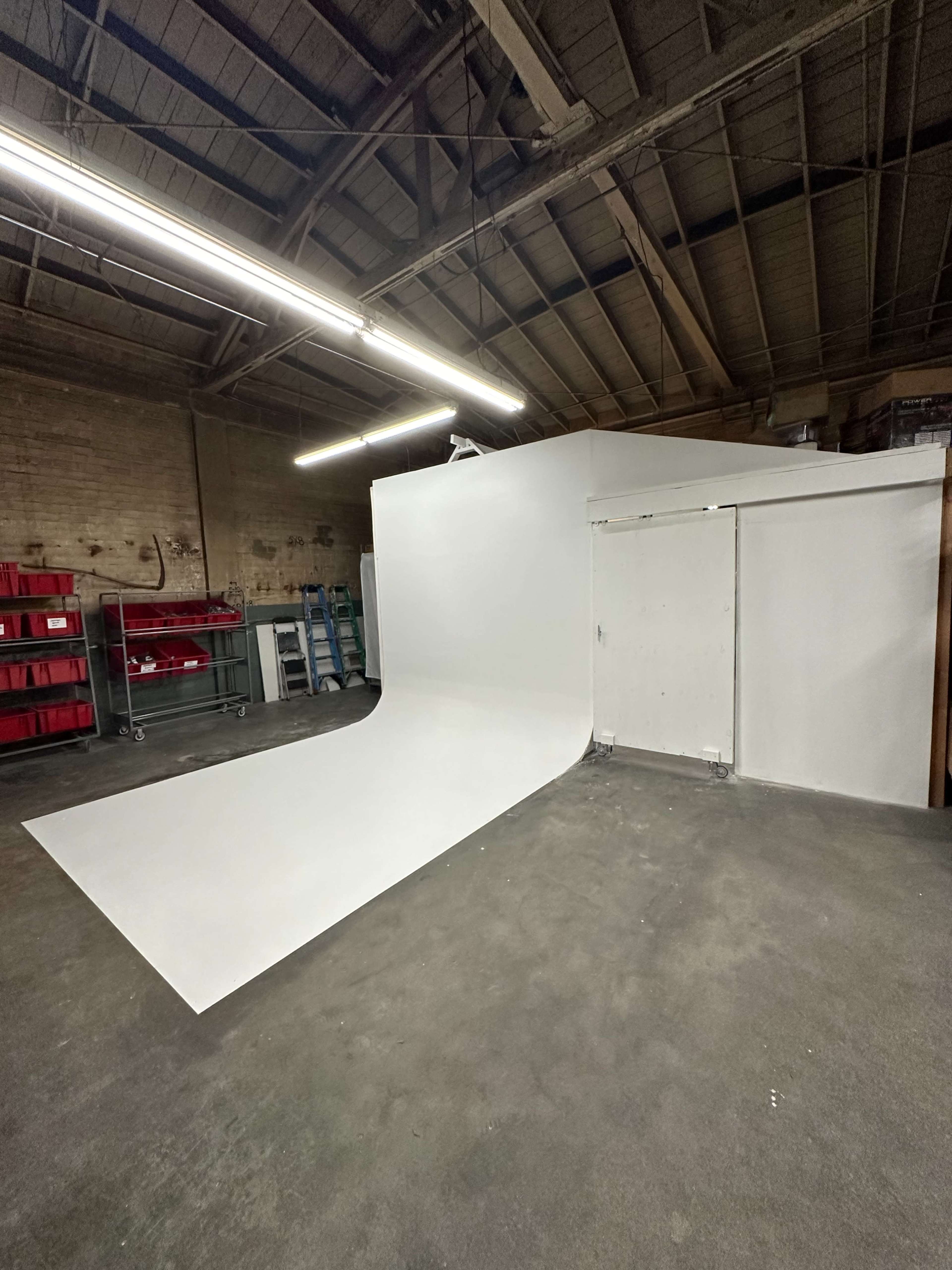 The image shows a spacious studio with a seamless white backdrop extending to the floor, surrounded by wooden beams and storage shelving.