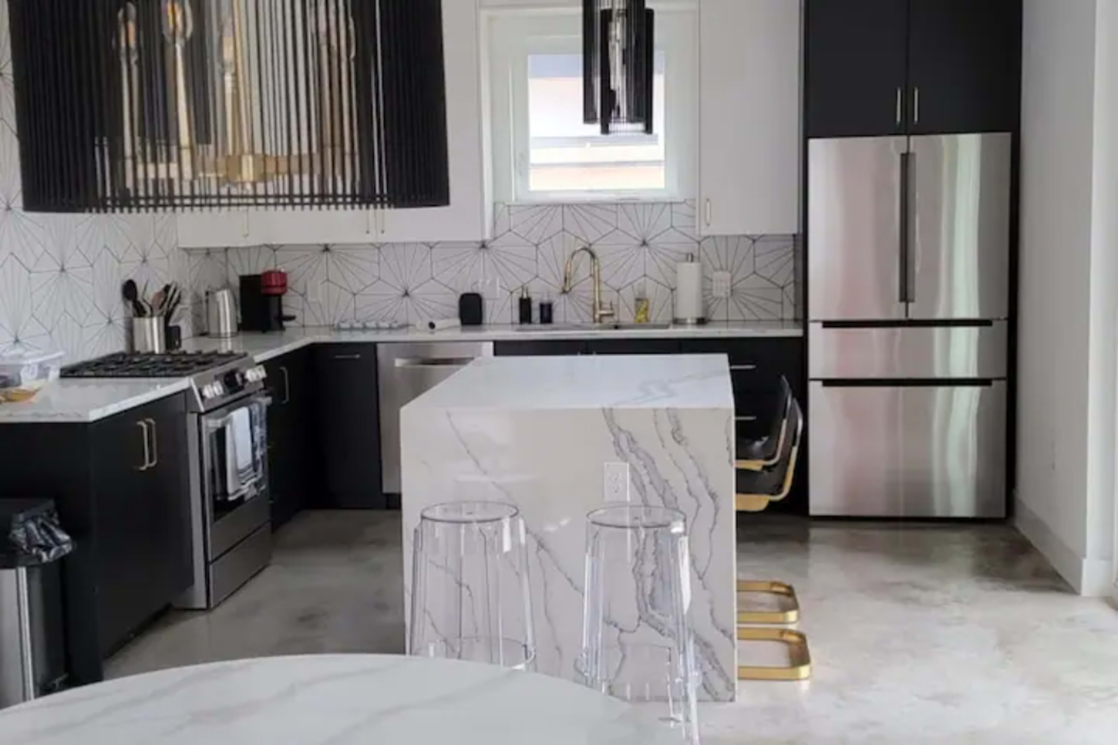 A modern kitchen features black and white cabinetry, a large marble island, and stainless steel appliances.