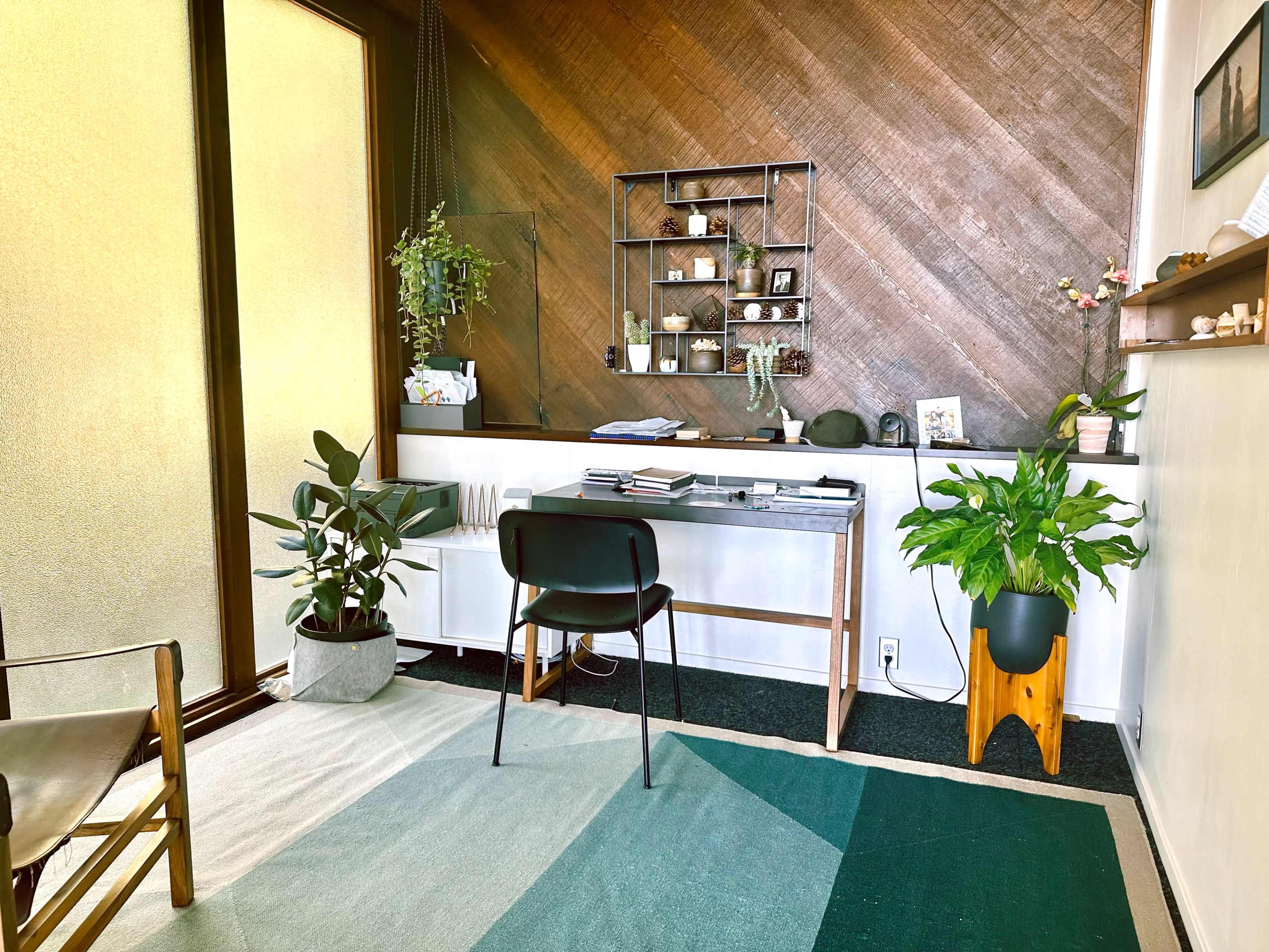 A modern workspace featuring a desk with neatly arranged items, plants, and a wall with a textured design.