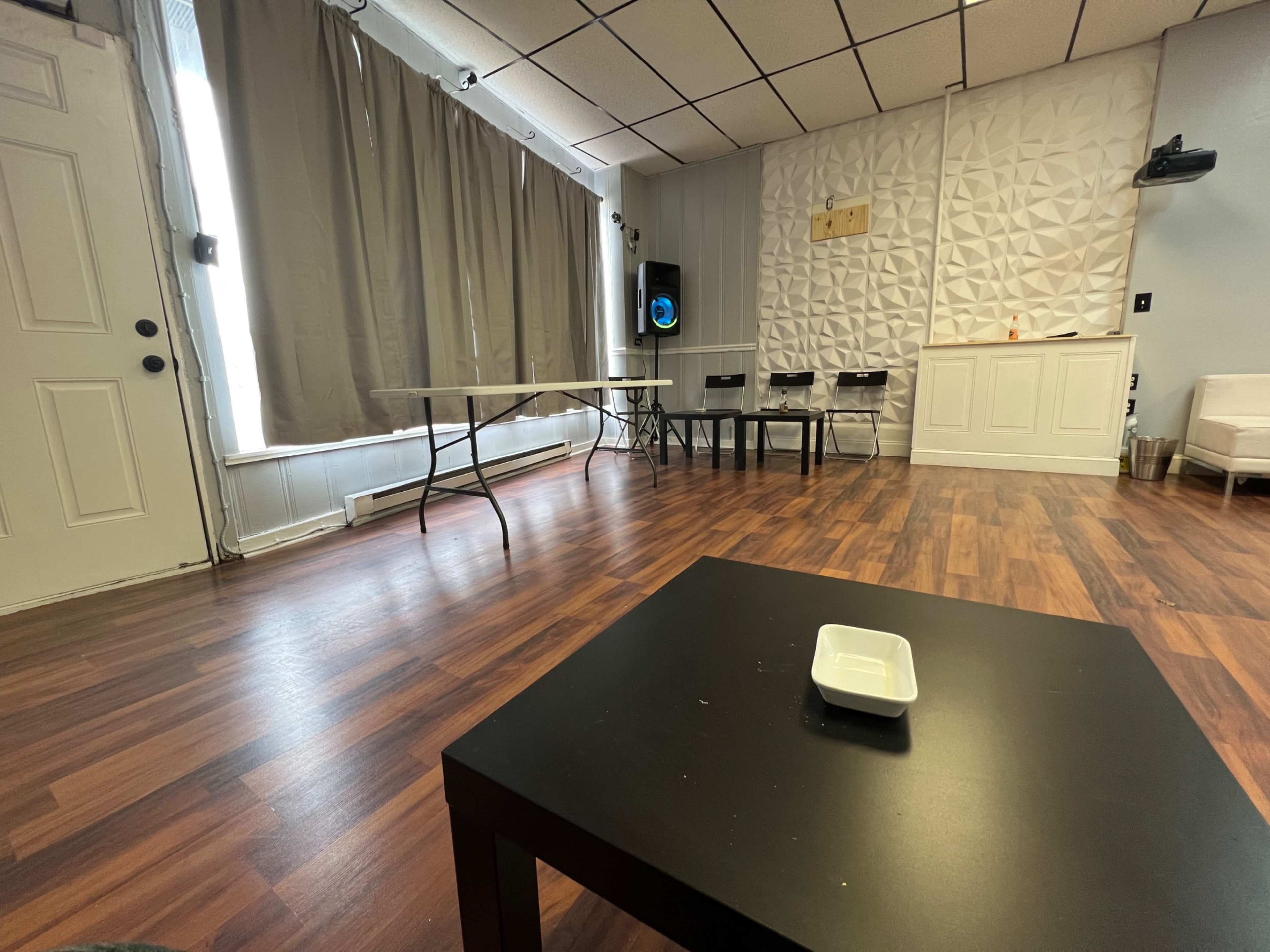 An empty room with wood flooring, a few tables and chairs, and a decorative wall feature.