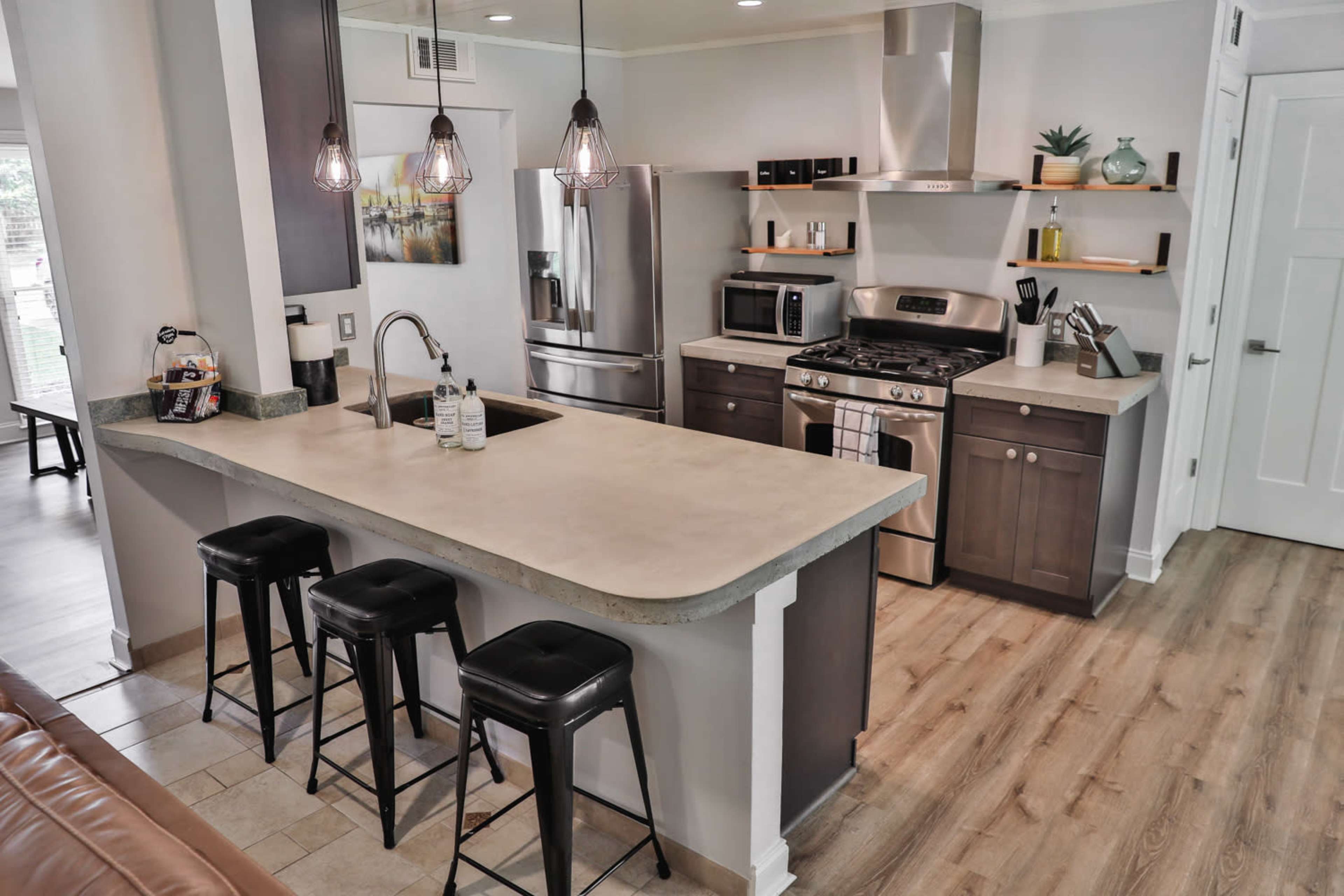 A modern kitchen with stainless steel appliances, a central island with seating, and wood laminate flooring.