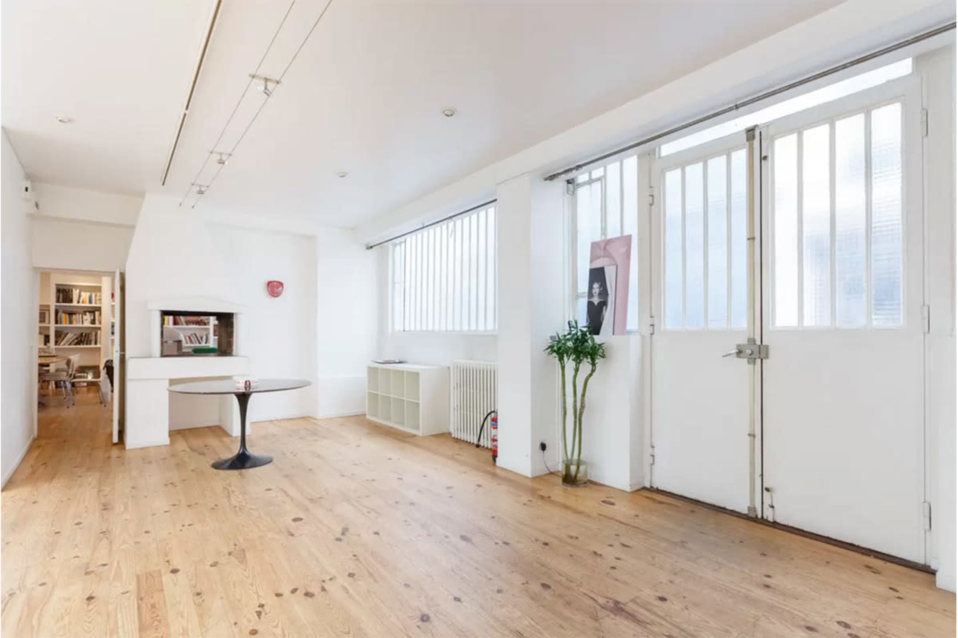 A bright, minimalistic room with wooden flooring, a round table, and large windows with metal frames.