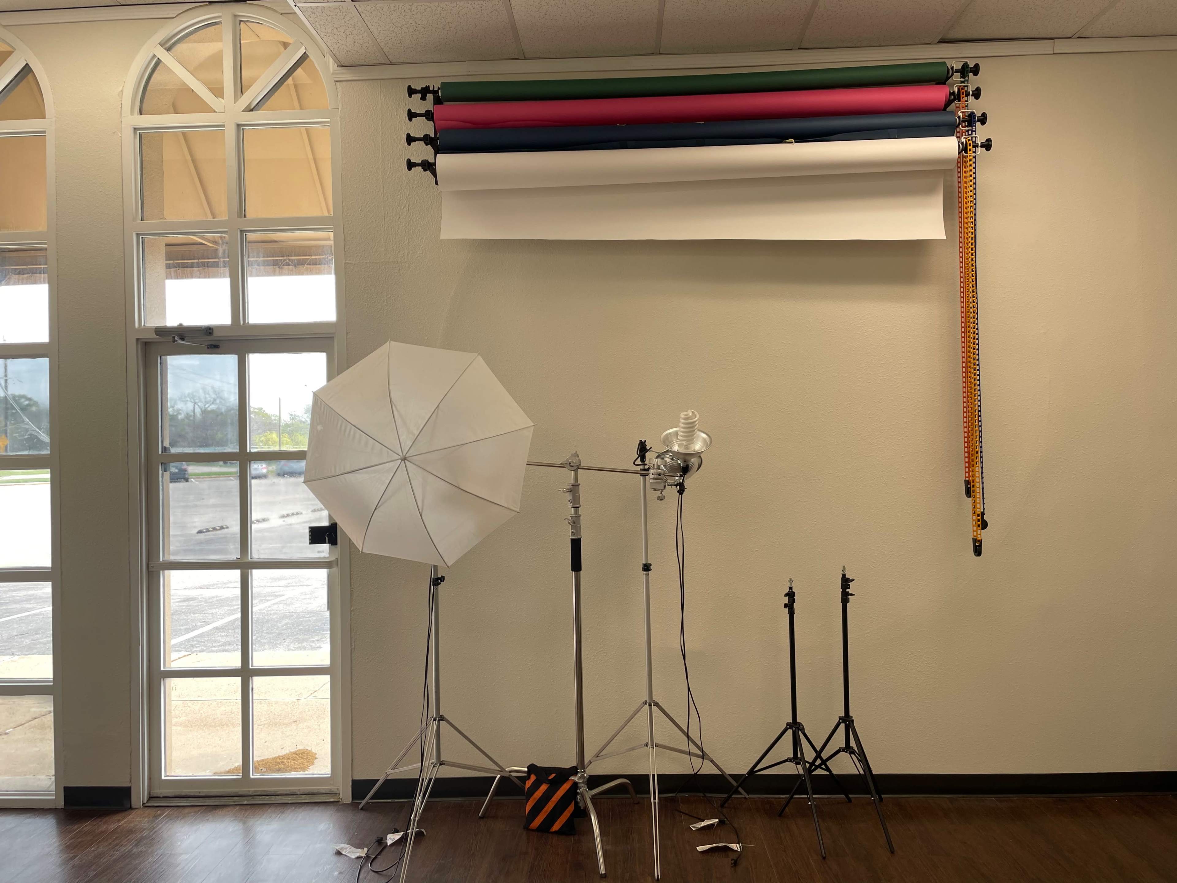 A photography studio setup with a light umbrella, a softbox, and several backdrops hanging on a wall.