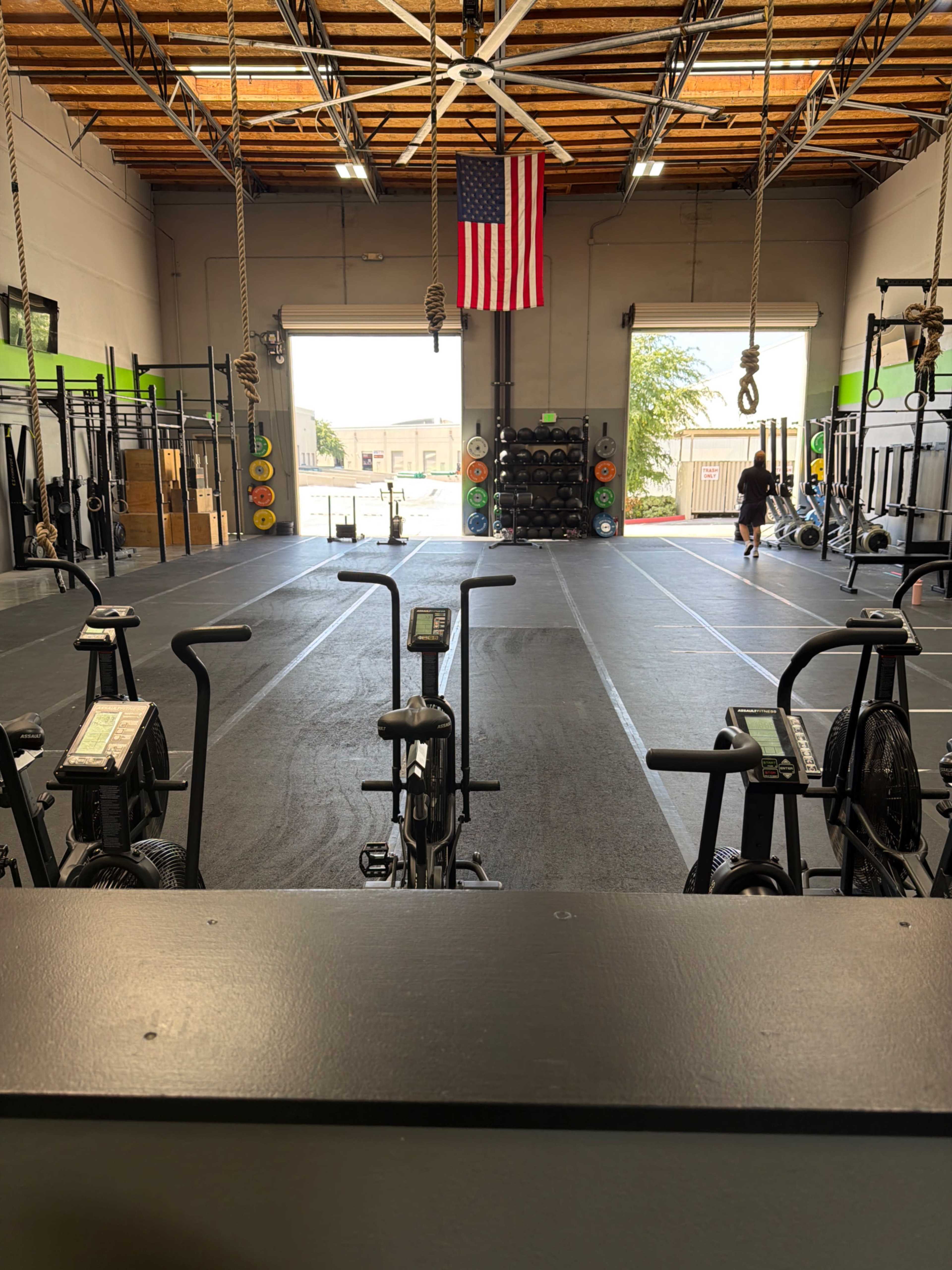 The image shows a spacious gym with exercise equipment facing an open area, featuring an American flag hanging near the entrance.