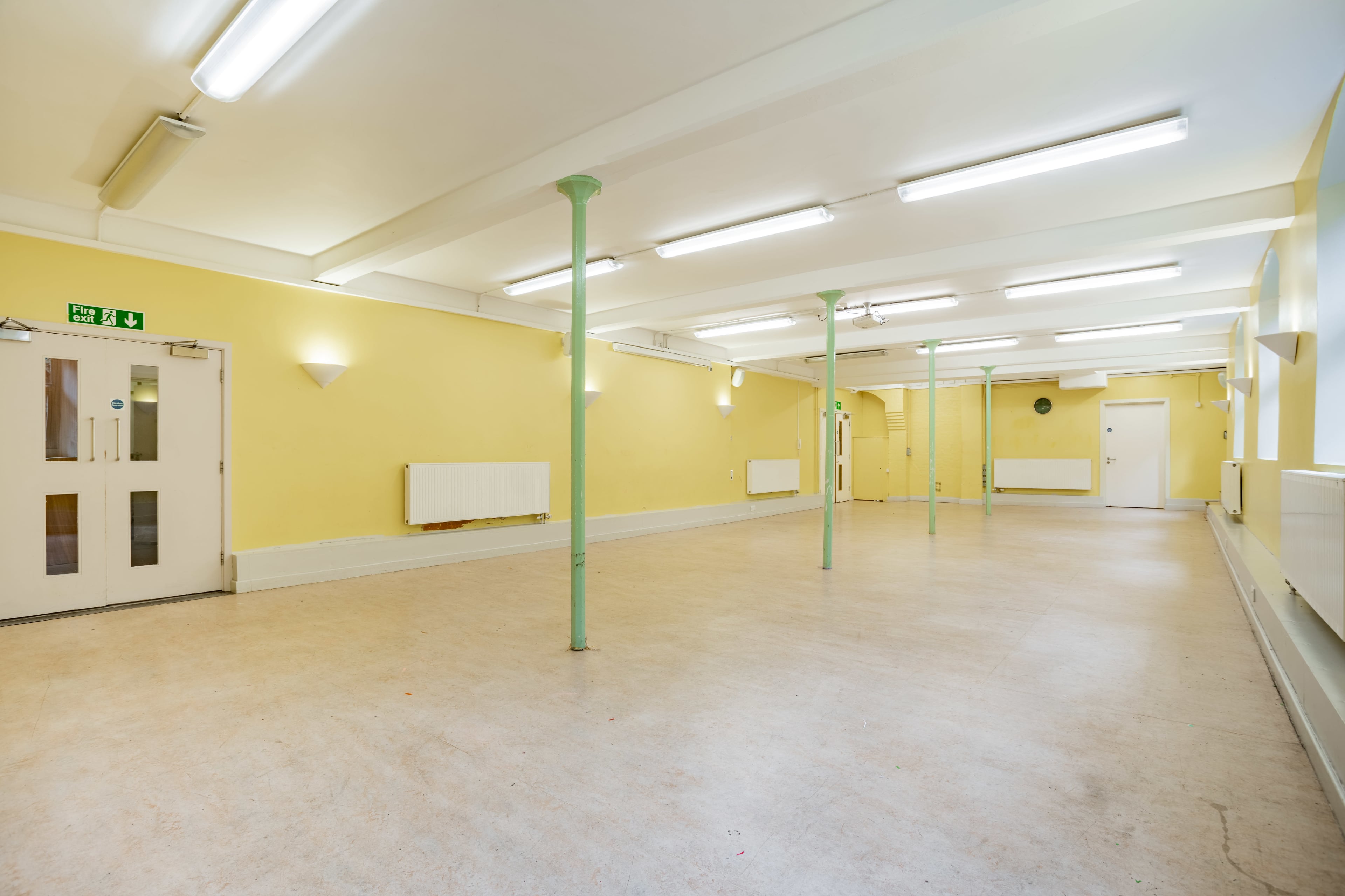An empty room with yellow walls, fluorescent lighting, and green support columns.