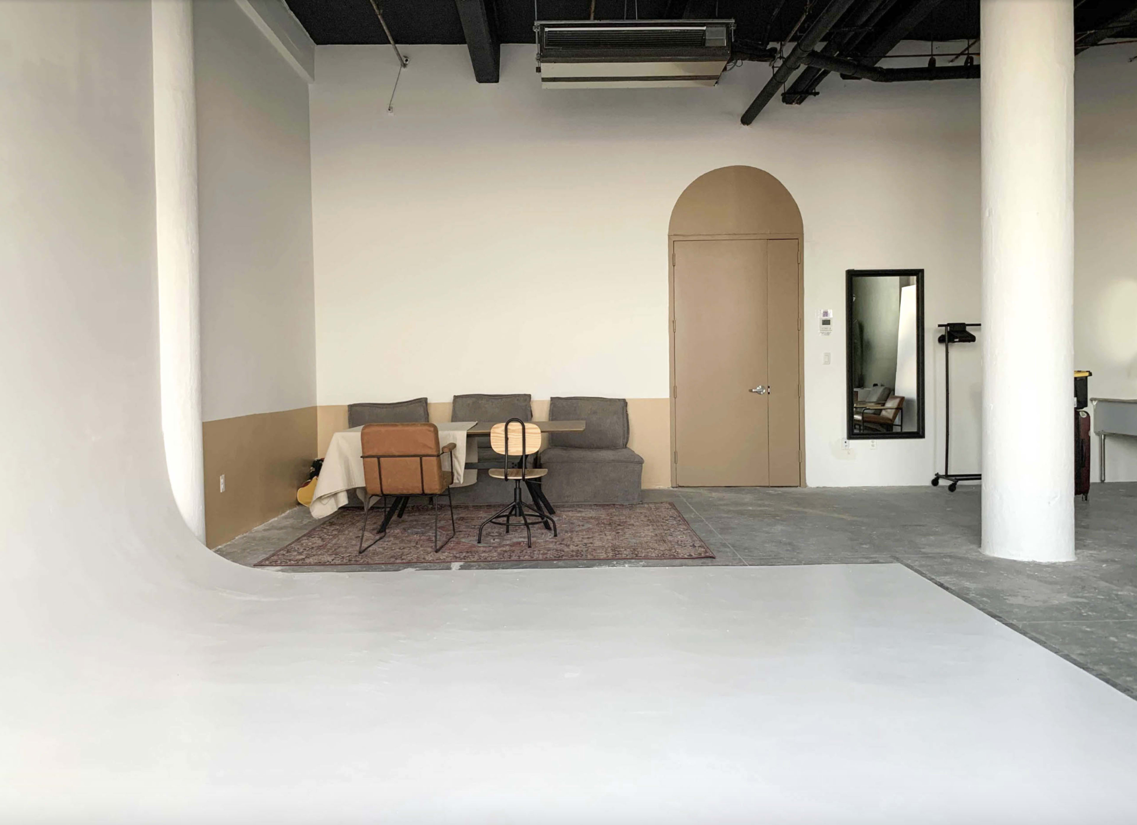The image shows a spacious studio interior with a white backdrop, a small seating area featuring a couch and chairs, and a mirror on the wall.