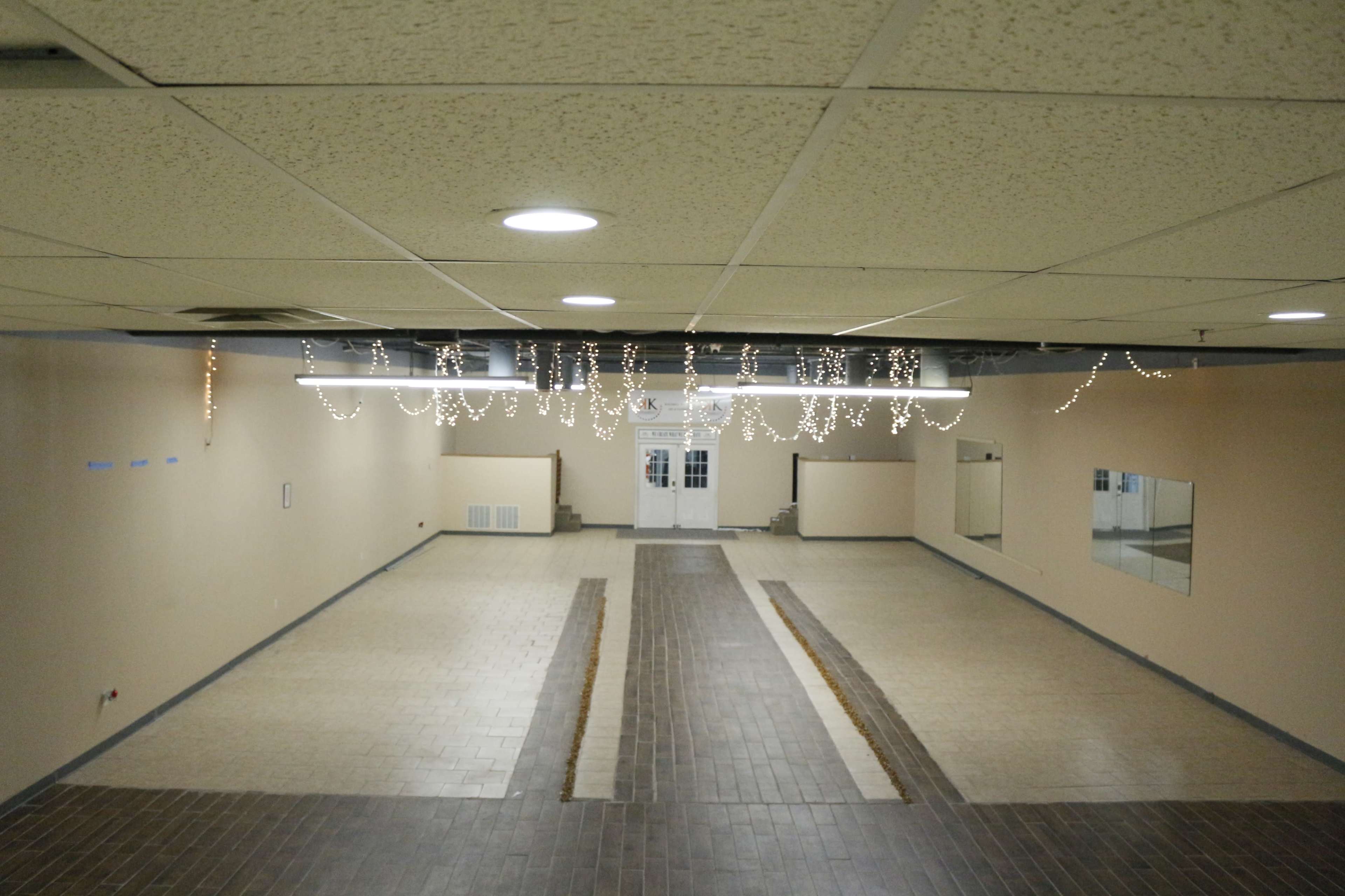 A spacious, empty interior room with tile flooring, featuring hanging decorative lights and multiple mirrors along the walls.