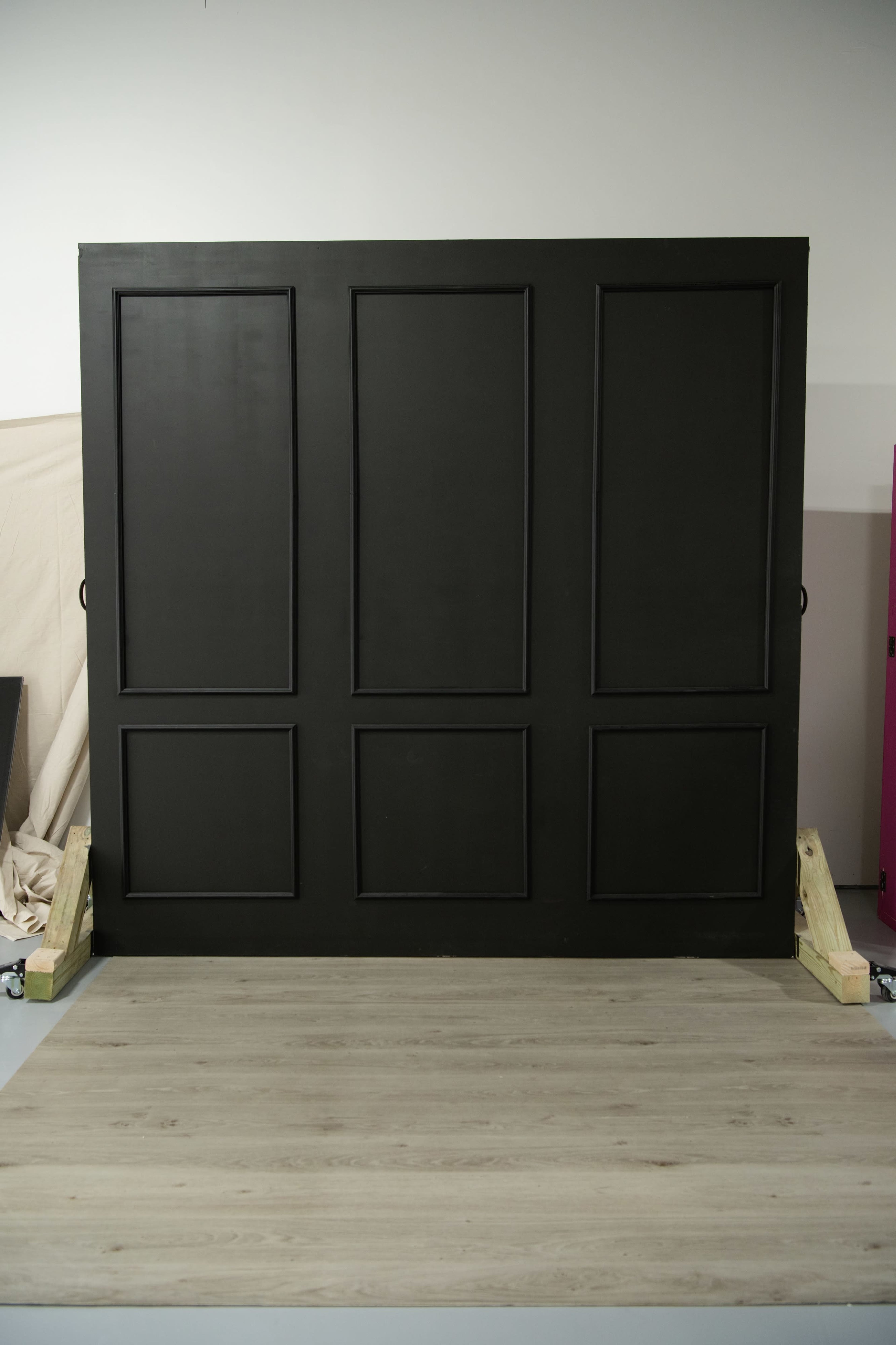 The image shows a large black wall with paneling and a light wooden floor in front of it.
