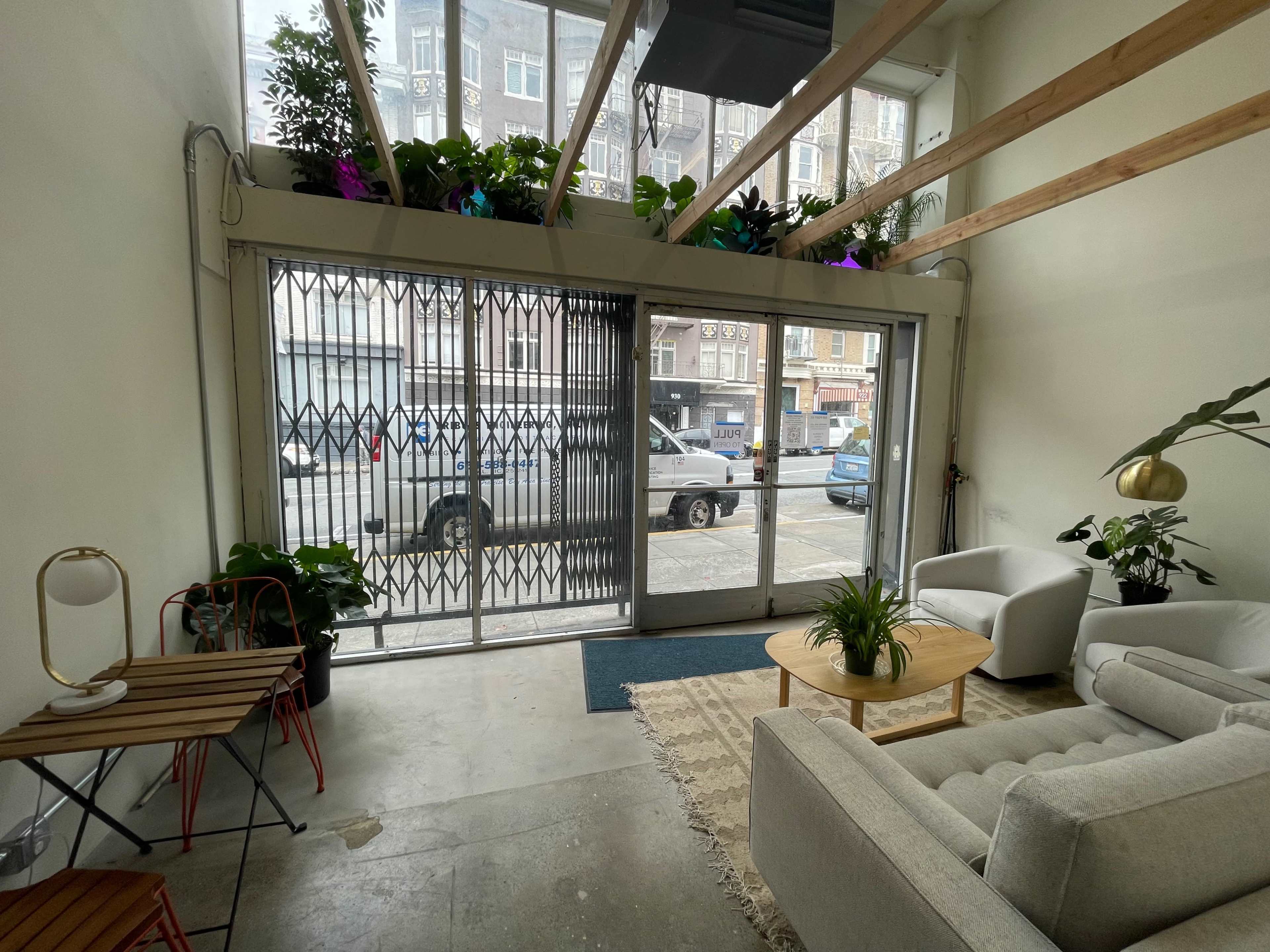 A minimalist interior space with a glass entrance, plants on the windowsill, a small wooden table with chairs, and a white sofa.