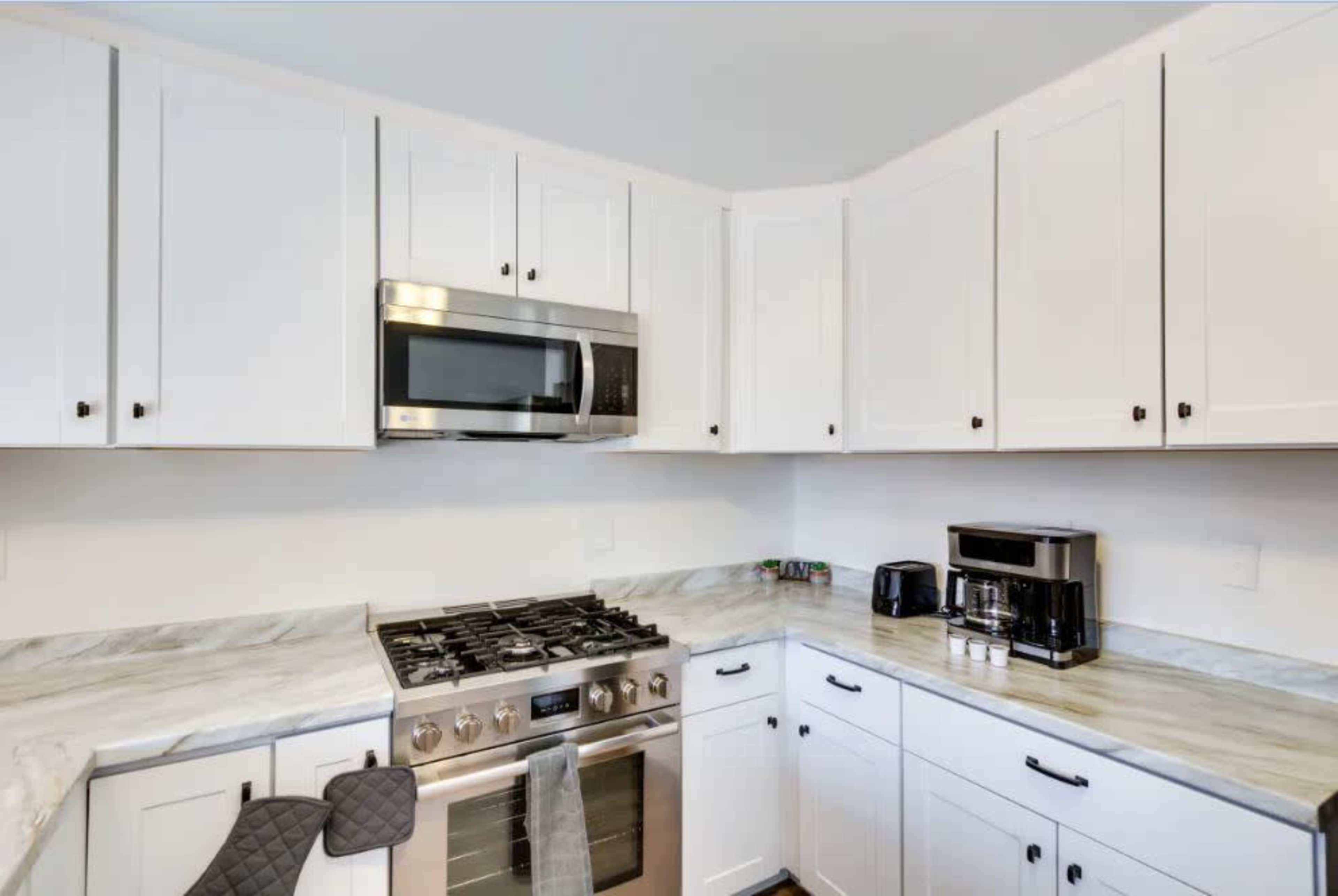 A modern kitchen features white cabinetry, stainless steel appliances, and a marble countertop.