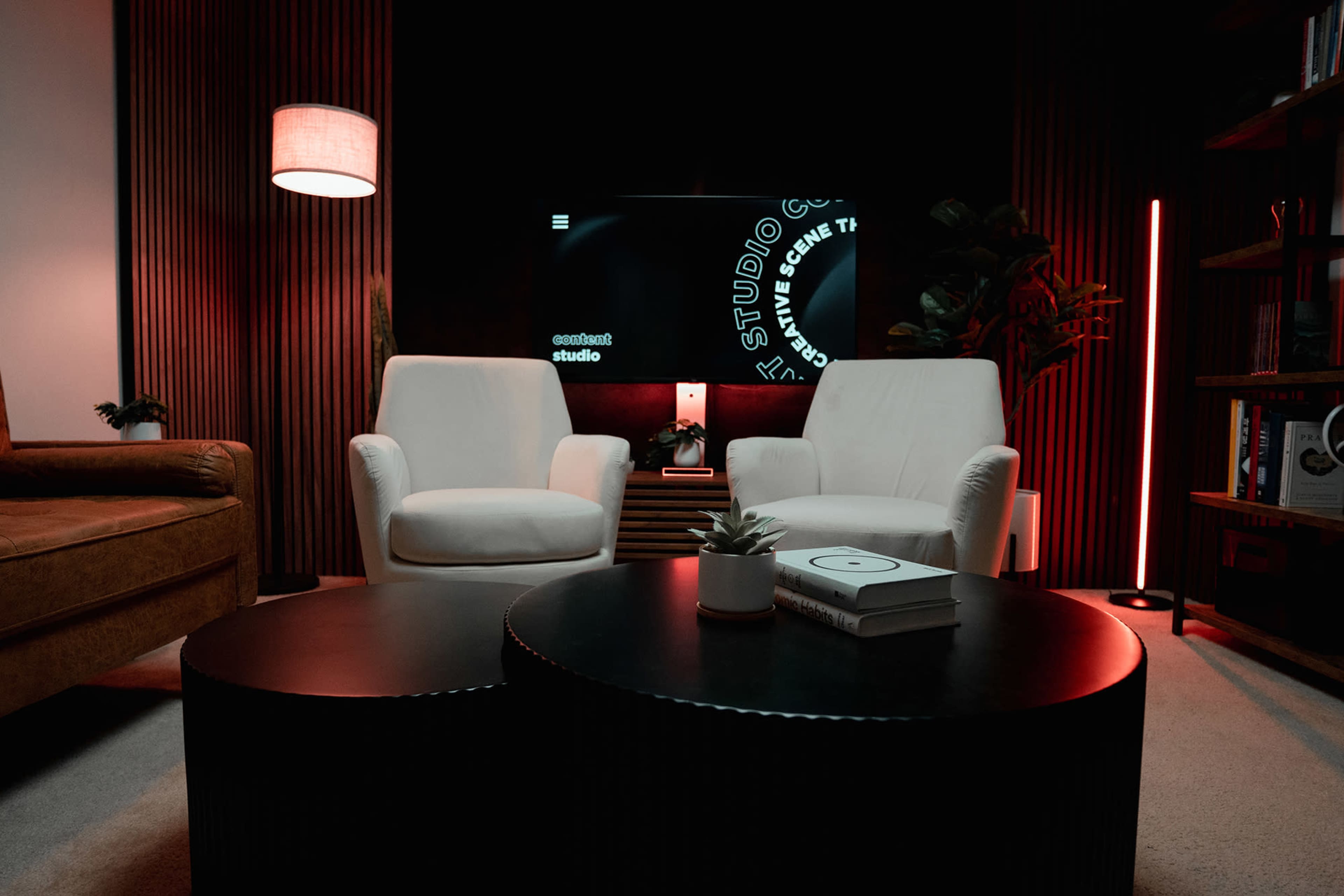 A modern living space with two white armchairs, a dark coffee table, a glowing floor lamp, and a television displaying design elements against a black backdrop.
