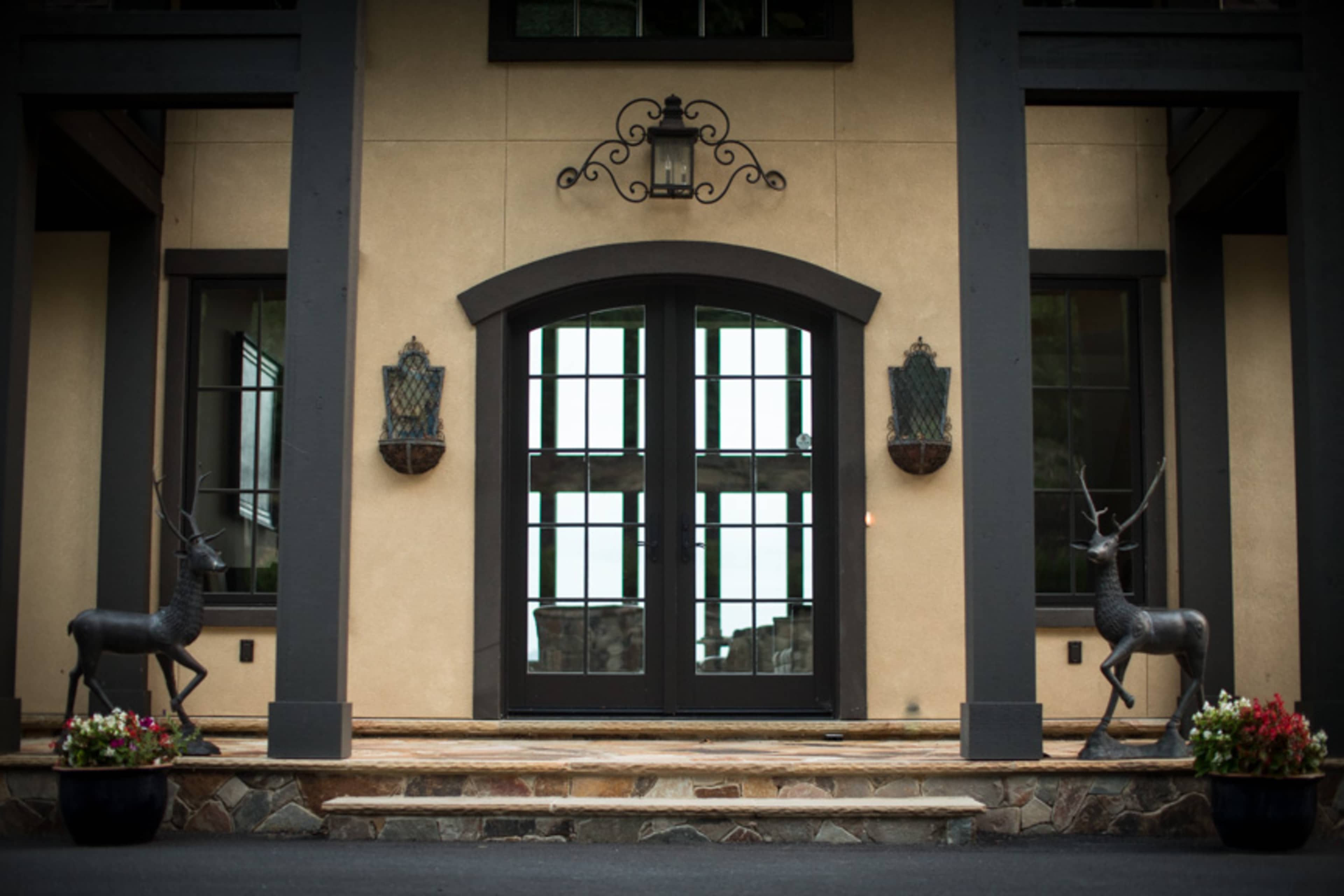 The entrance features double black doors flanked by two decorative deer statues and planters with flowers.