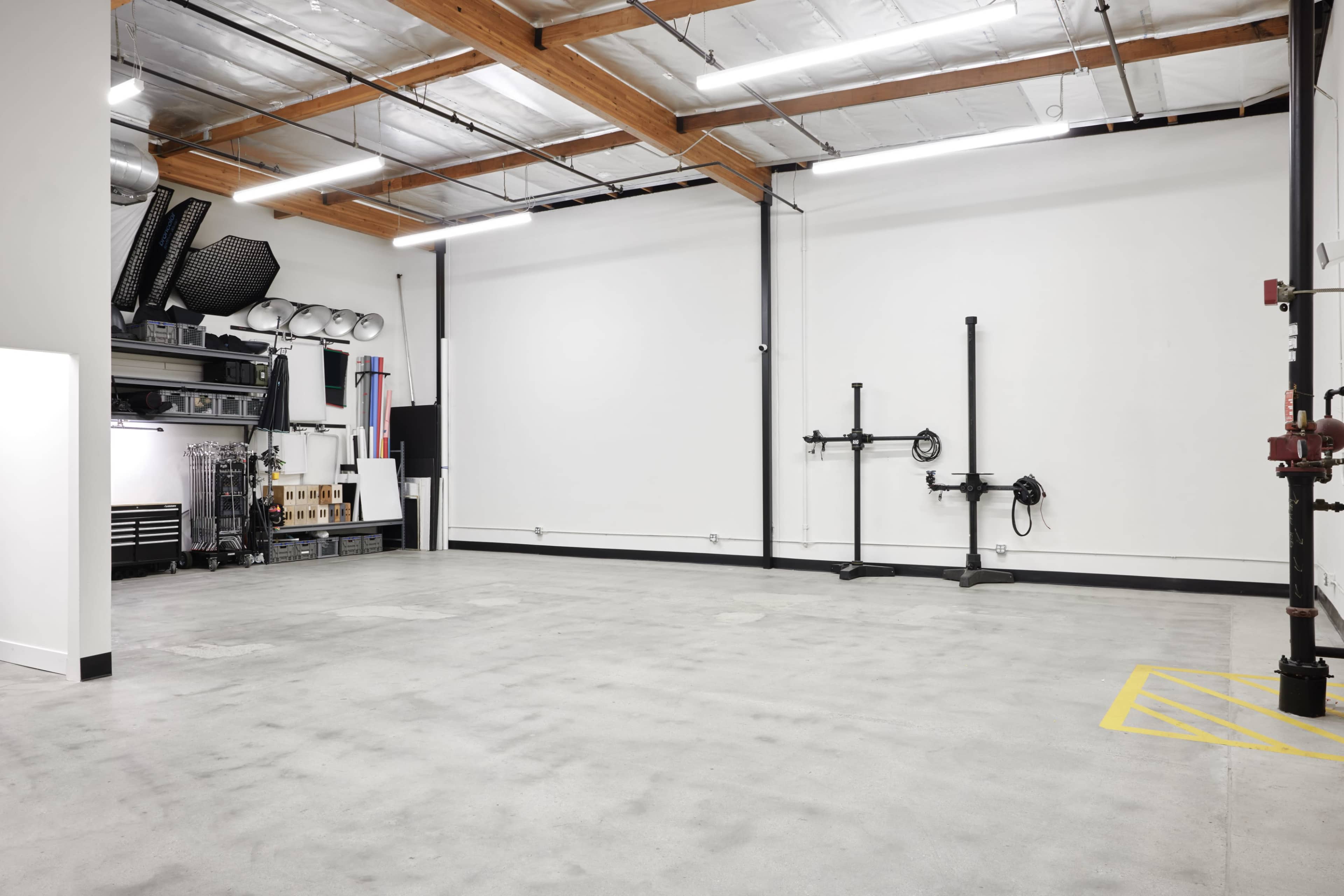 The image shows a spacious, empty garage or workshop with a polished concrete floor, white walls, and industrial lighting.