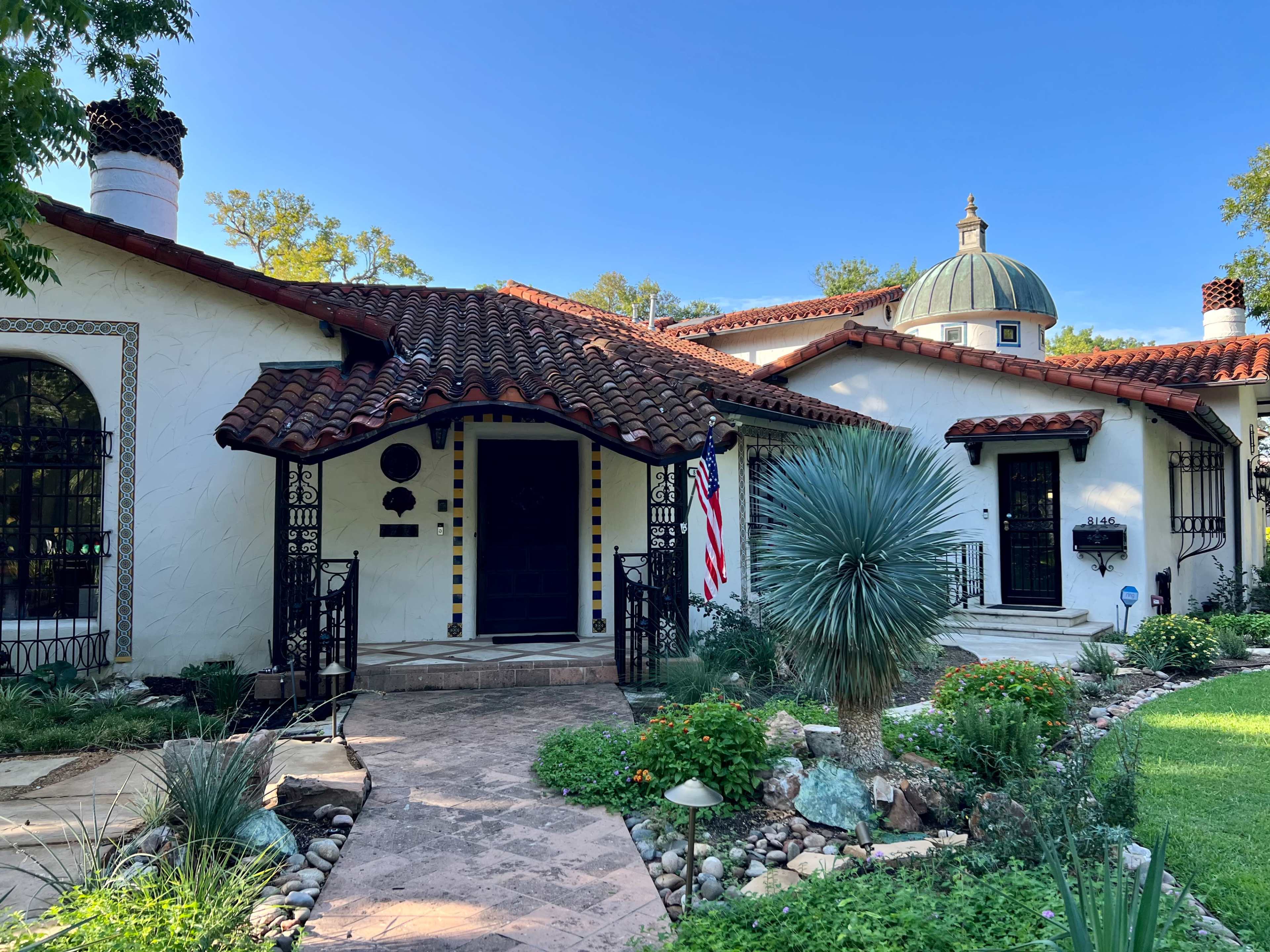 A Spanish-style house with a domed roof, surrounded by a lush garden and walkway leading to the entrance.