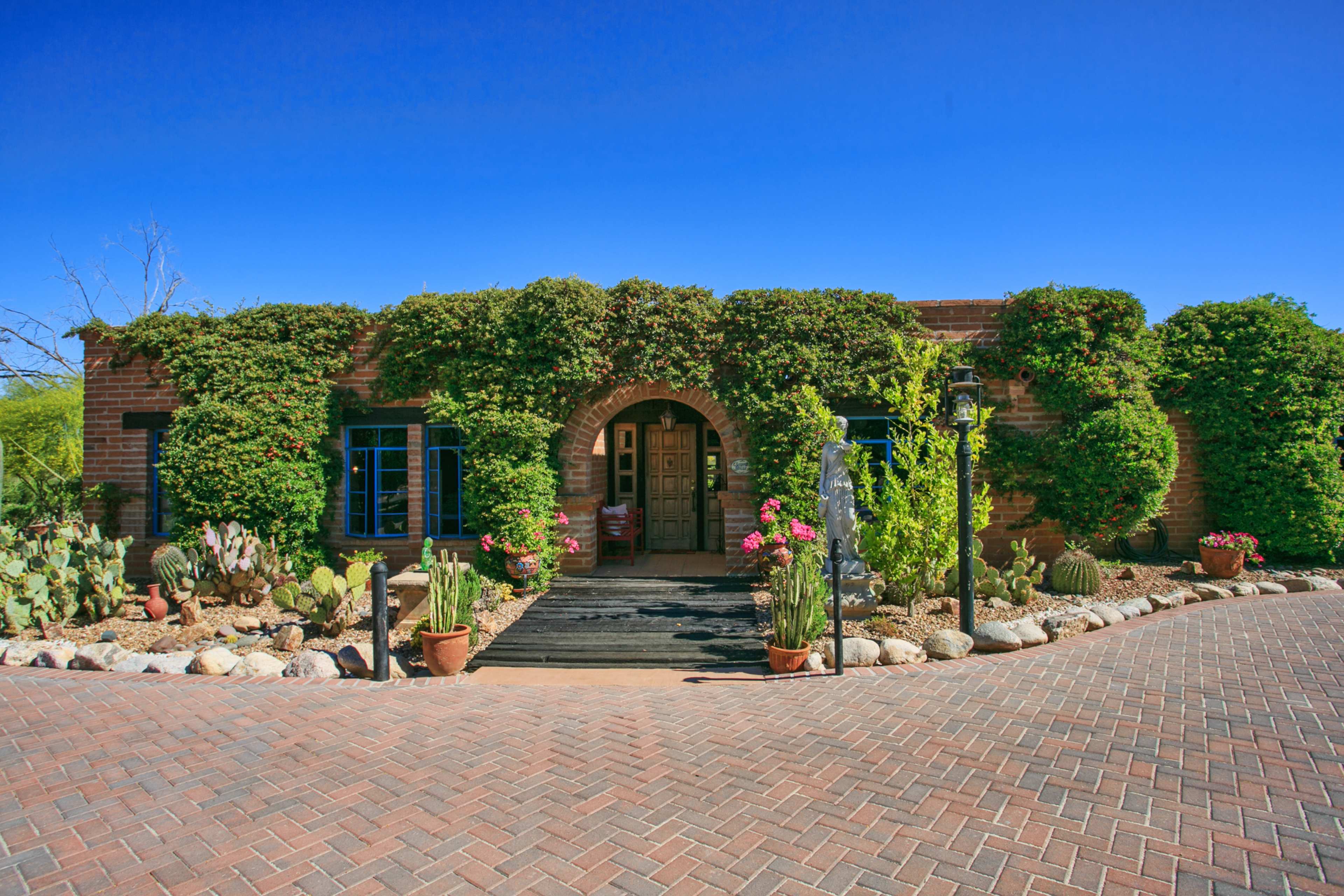 A brick home with a large entrance arch is surrounded by greenery and colorful plants along a patterned pathway.