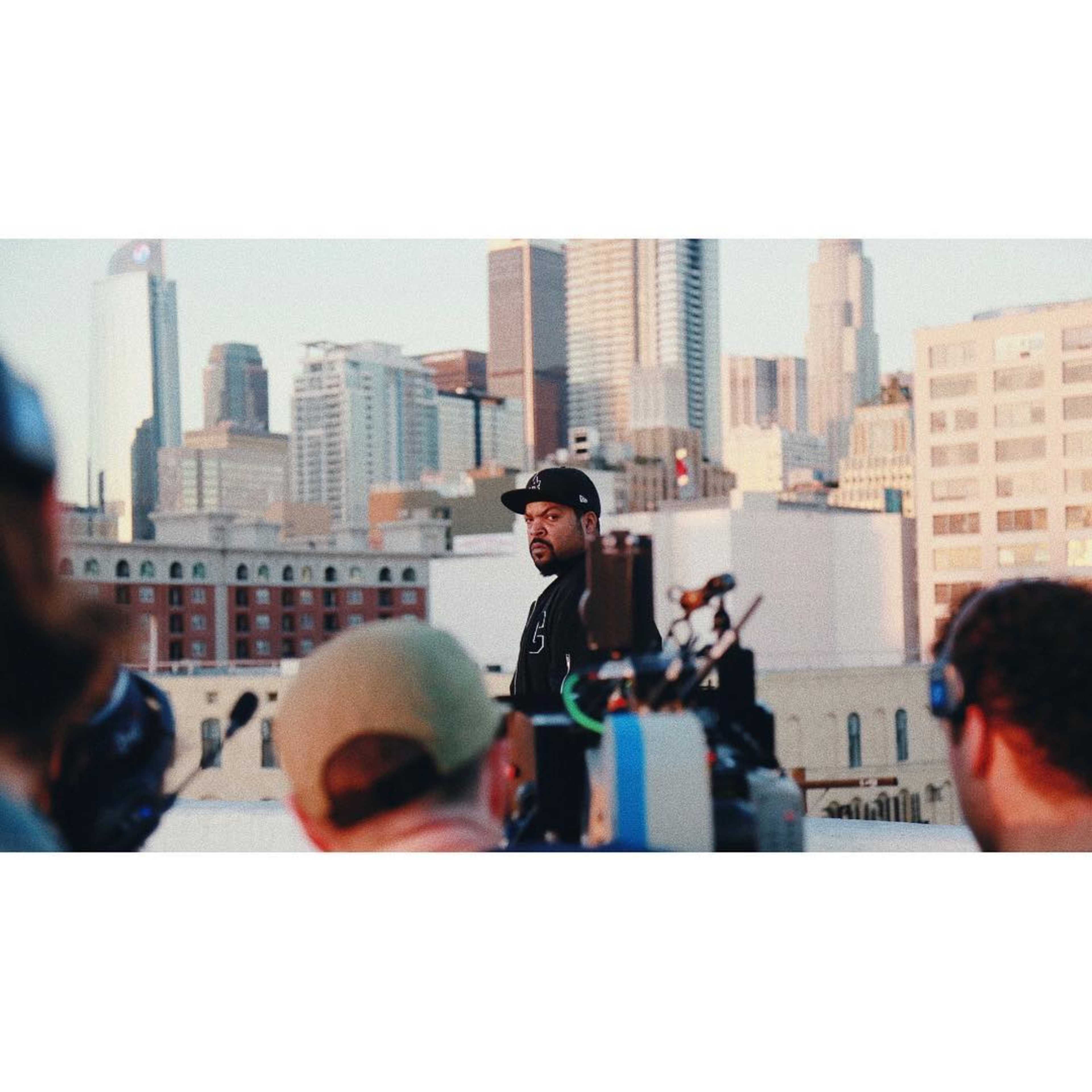 A man stands on a rooftop overlooking a city skyline, surrounded by film crew equipment.