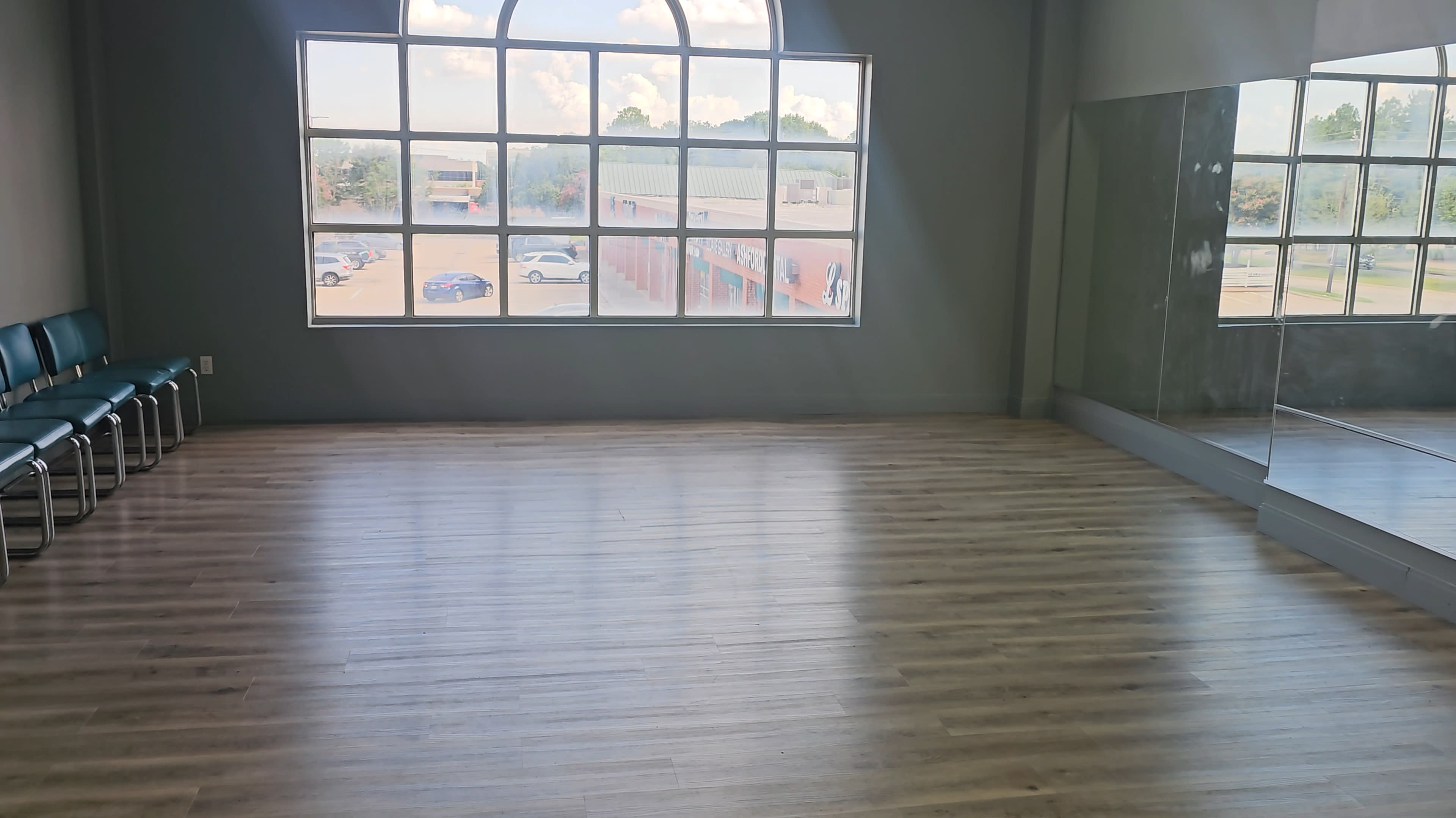 A spacious room with wooden flooring and a large arched window letting in natural light.