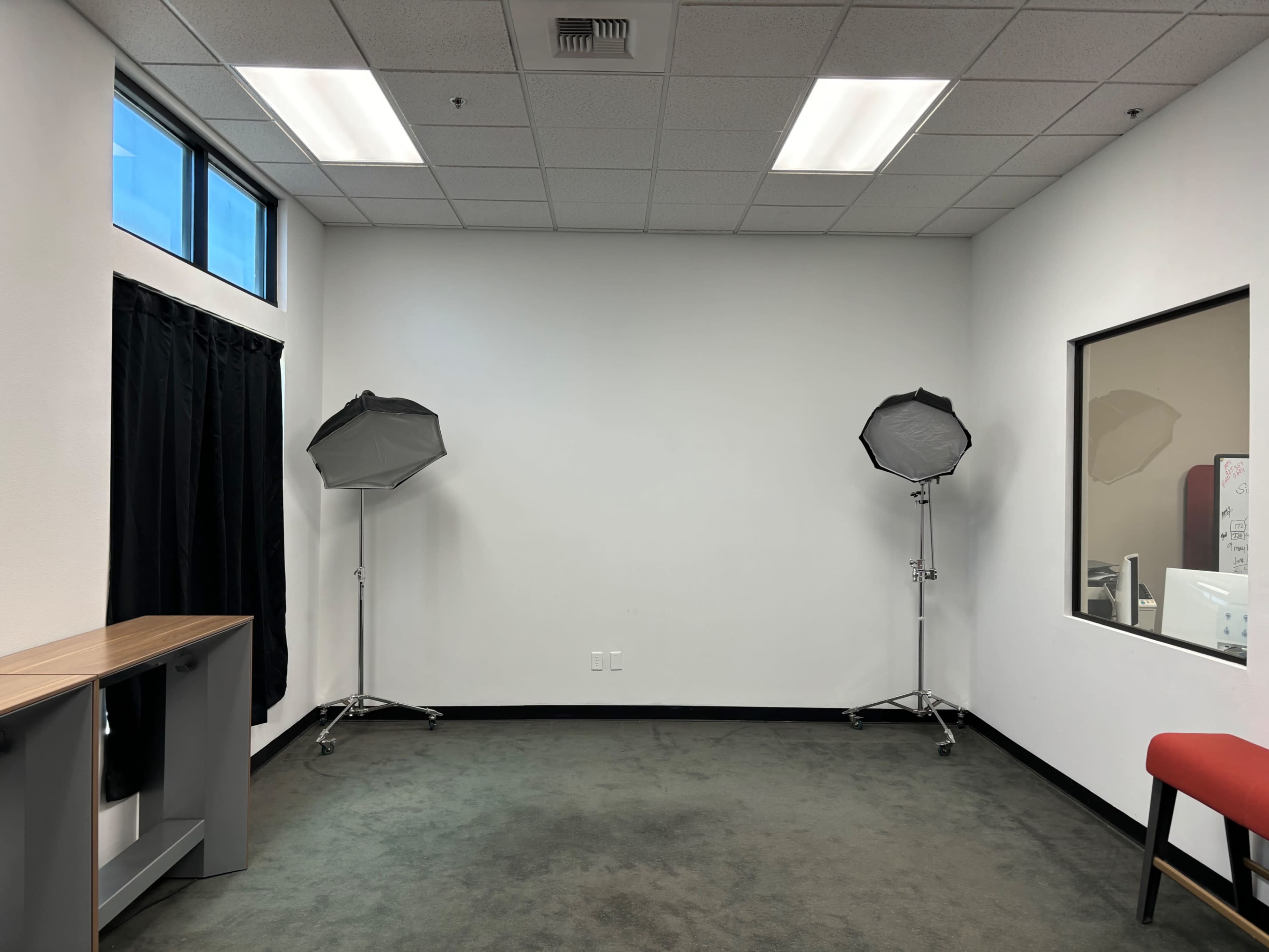The image shows an empty room with two lighting fixtures on stands, a window on one side, and a desk against the wall.