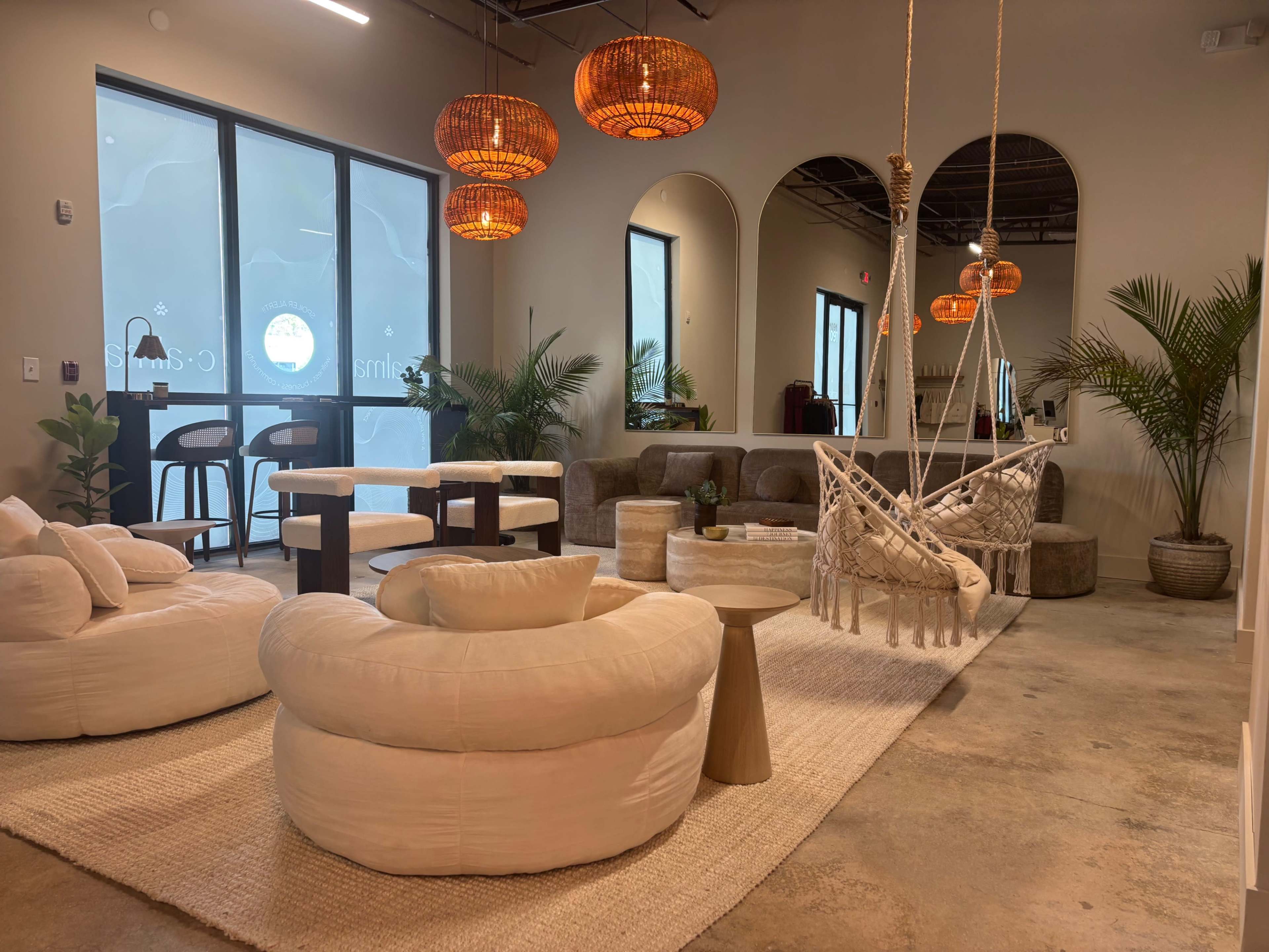 The scene depicts a modern indoor lounge area featuring circular sofas, a macramé swing, stylish lighting, and potted plants.
