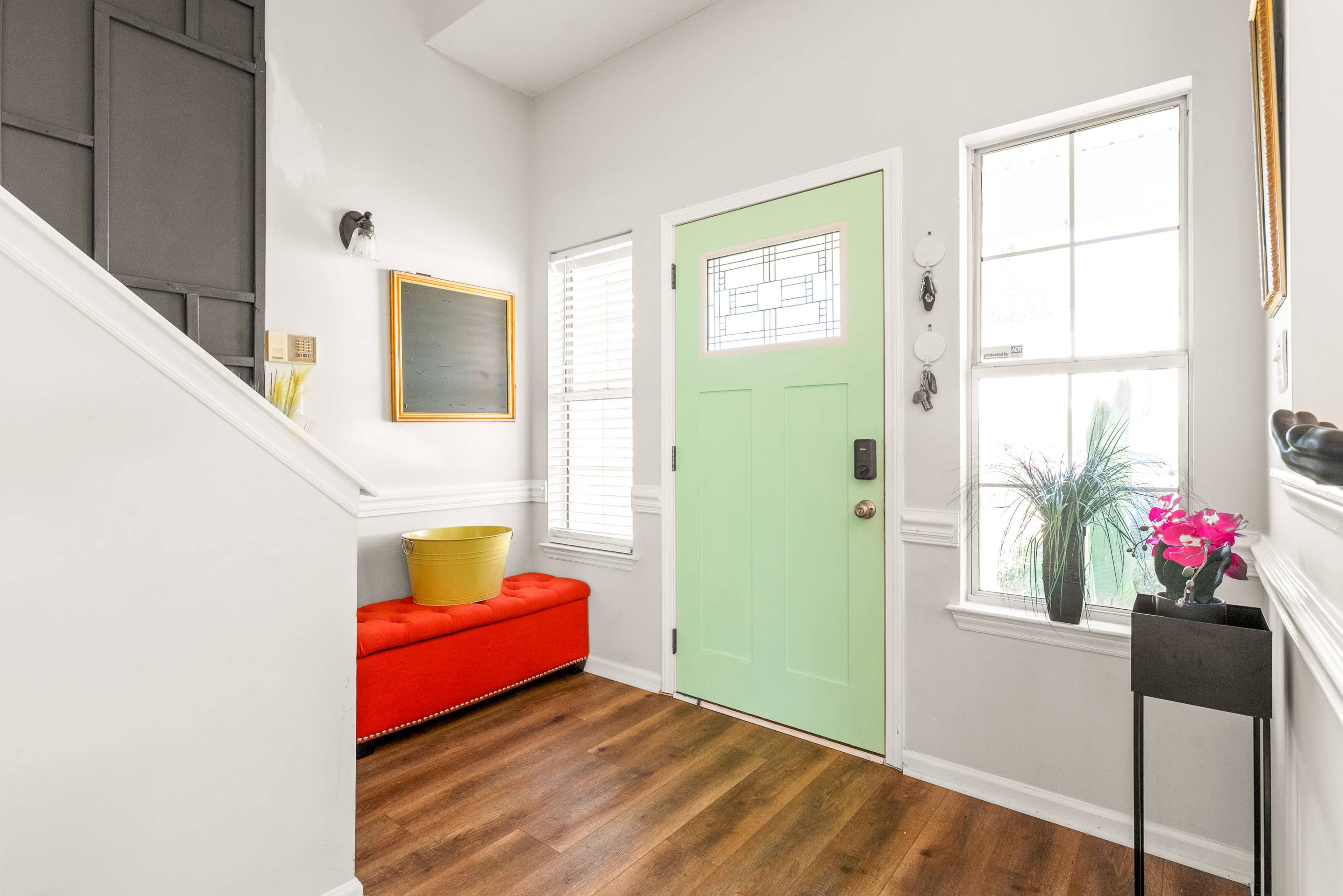 The entryway features a mint green front door, a red bench, and large windows that allow natural light to enter.