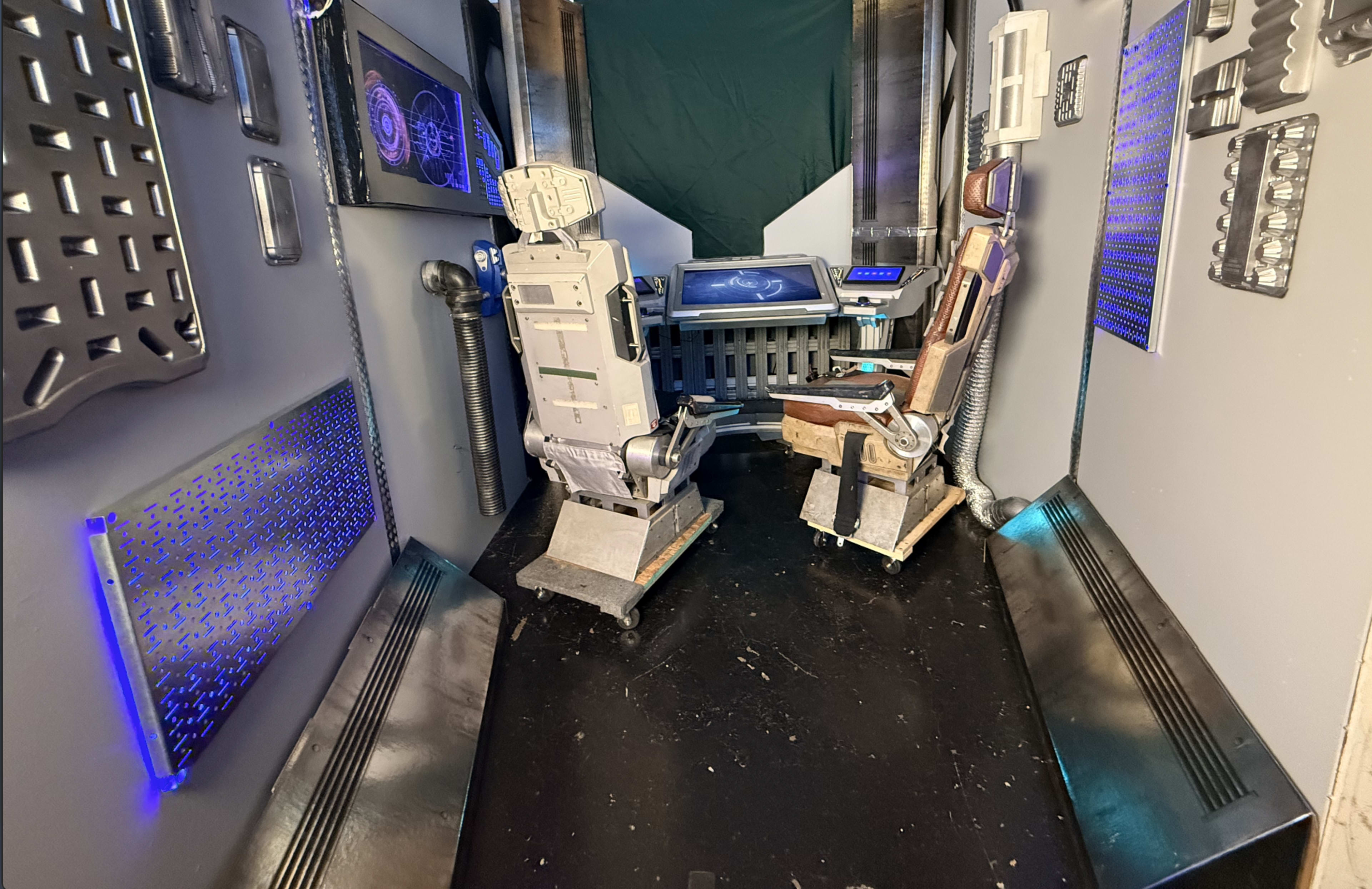 The image shows a futuristic control room with two high-tech chairs and various metallic panels integrated into the walls.