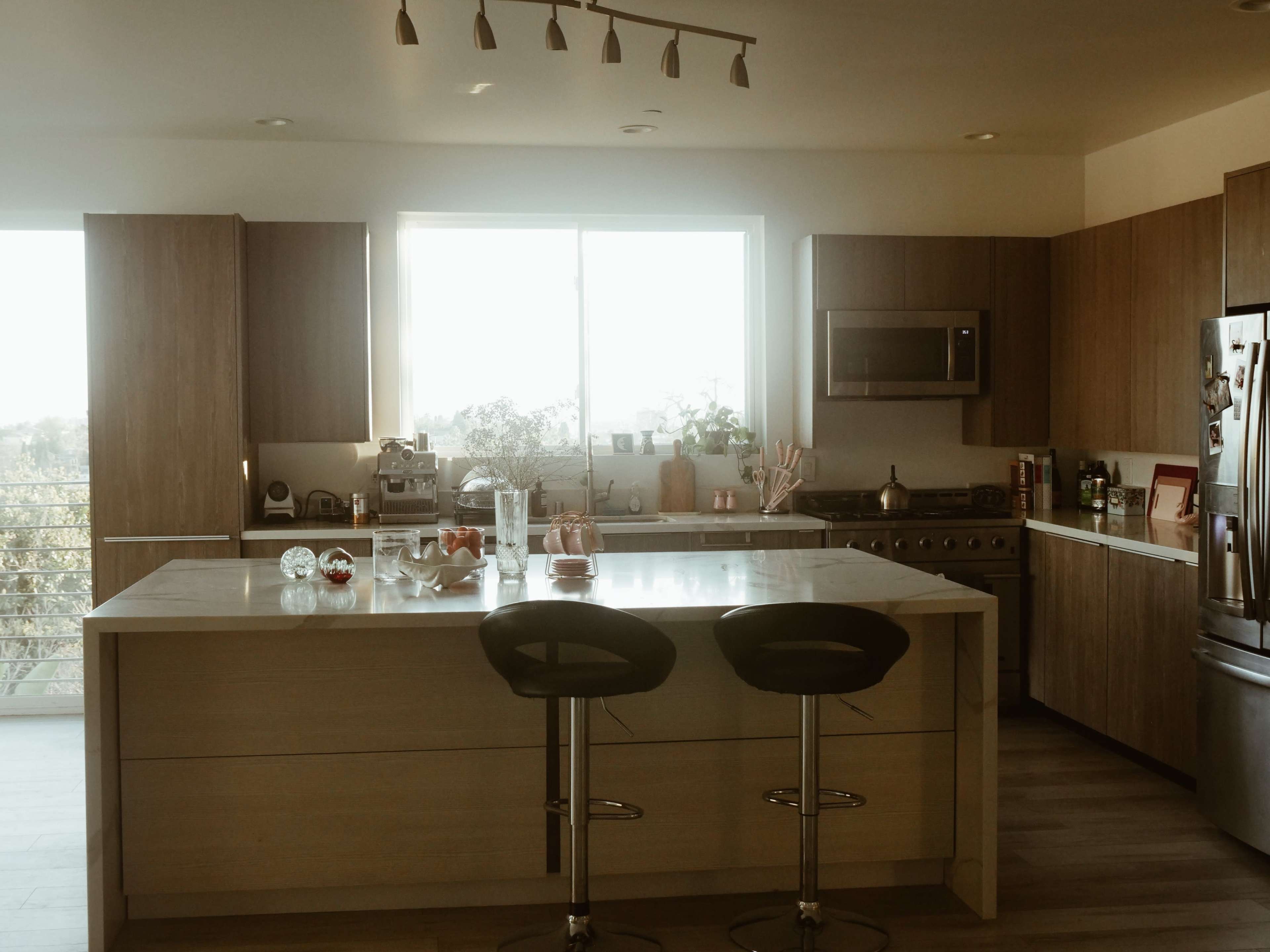 A modern kitchen features a large island with bar stools, stainless steel appliances, and a large window letting in natural light.