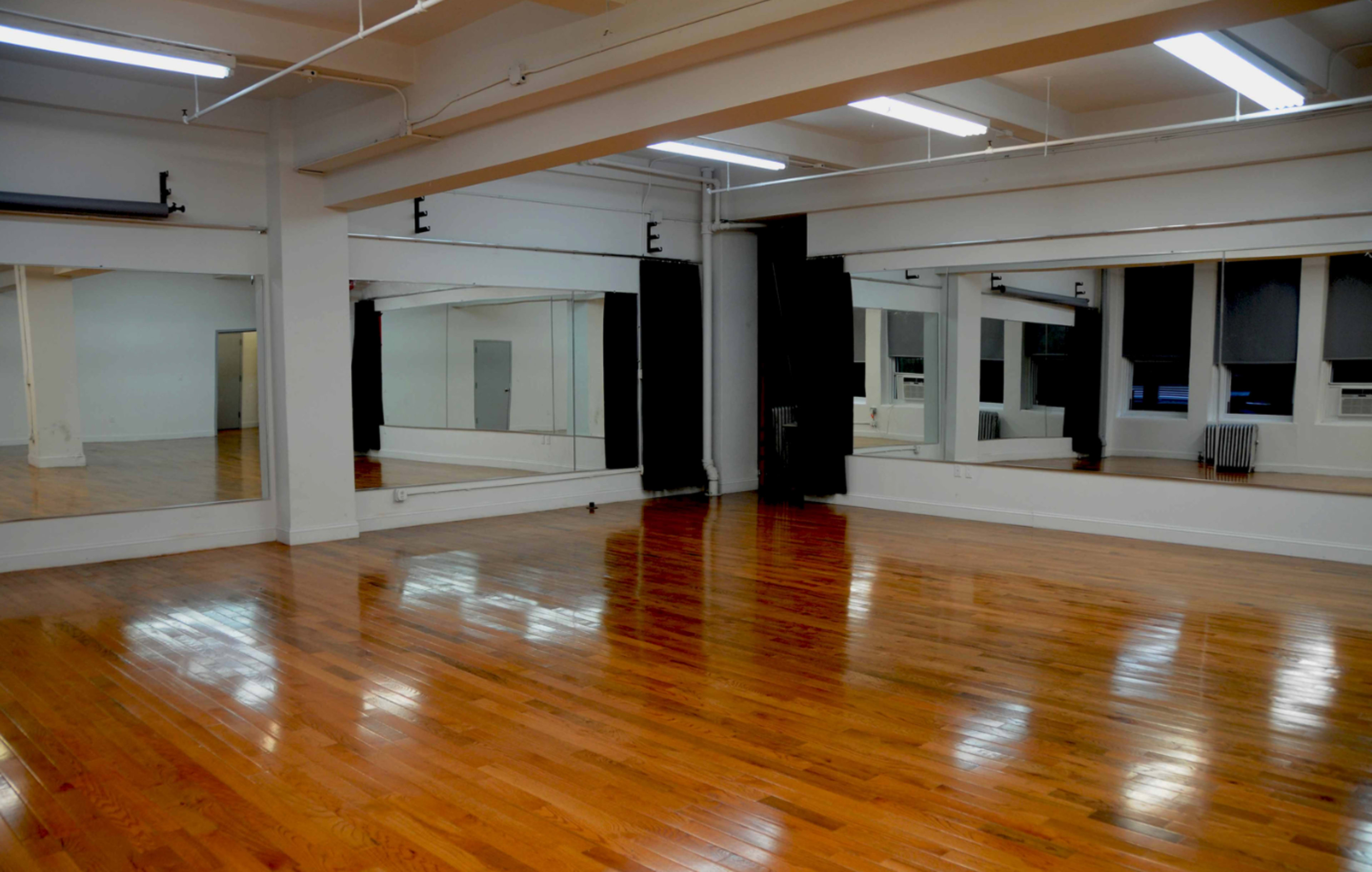 A spacious dance studio with polished wooden floors and large mirrors on the walls.