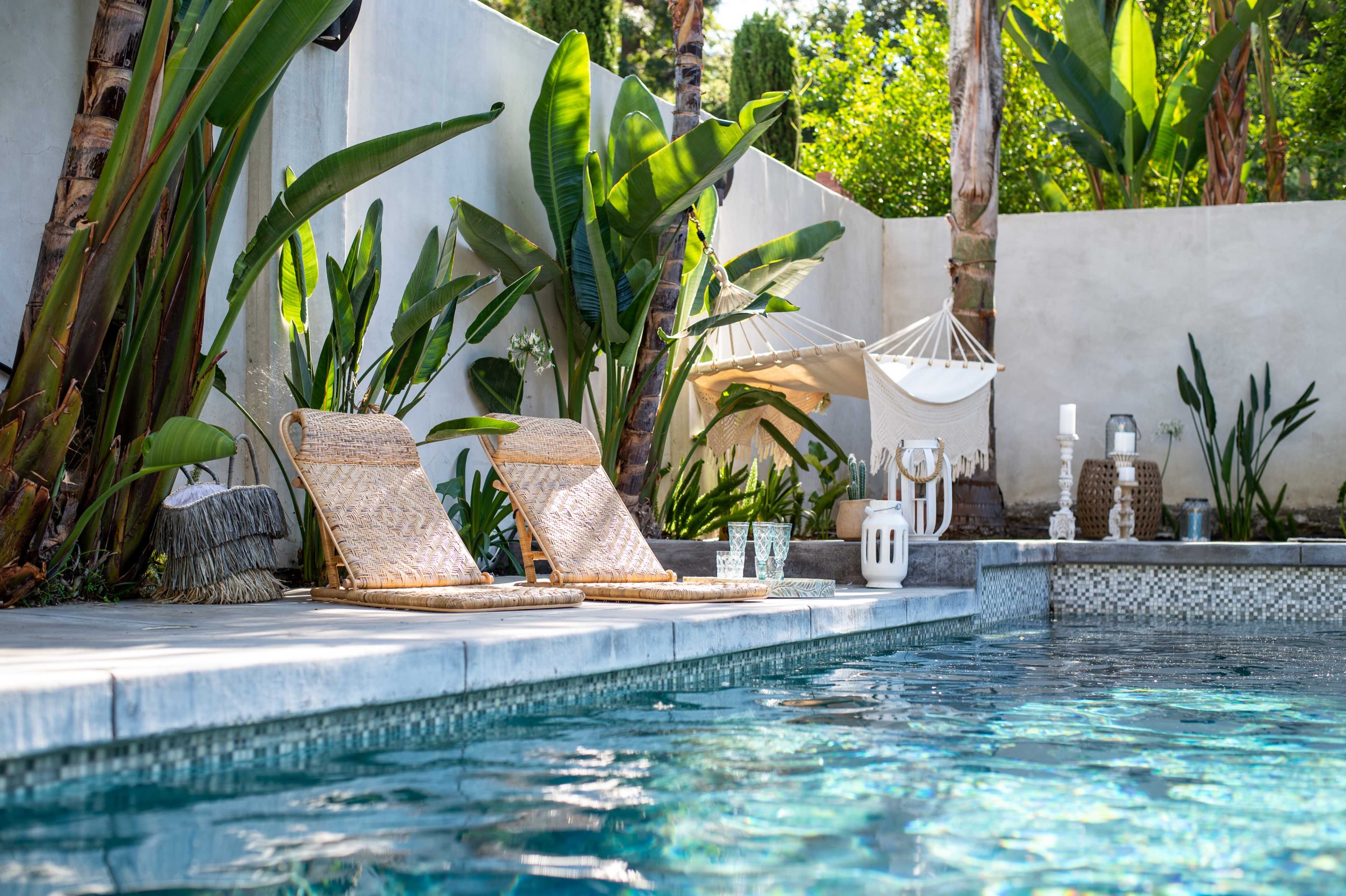 A serene swimming pool area features two lounge chairs beside the water, surrounded by lush greenery and decorative elements.