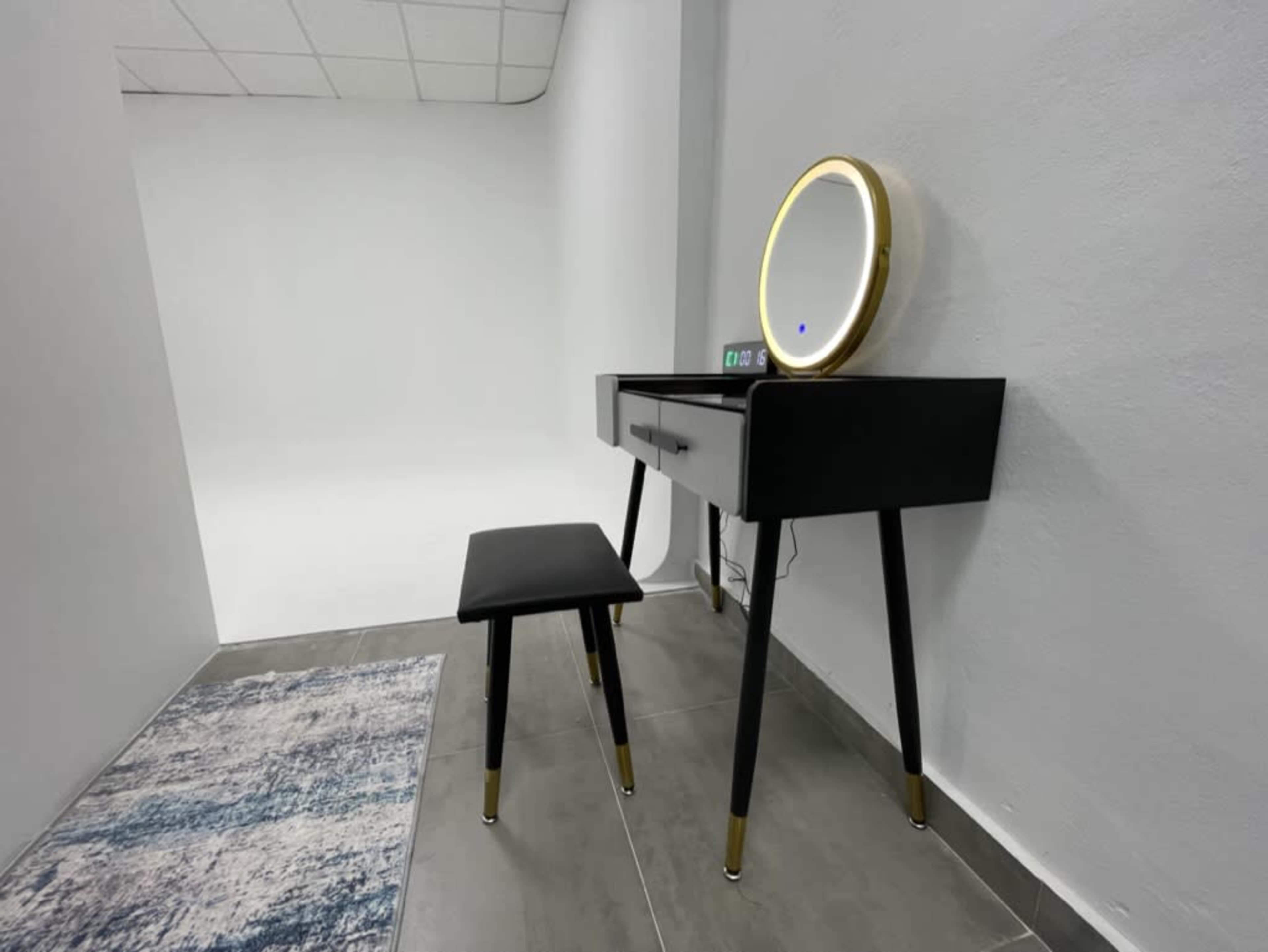 A modern vanity table with a circular mirror and a black stool sits against a neutral wall in a minimalistic room.
