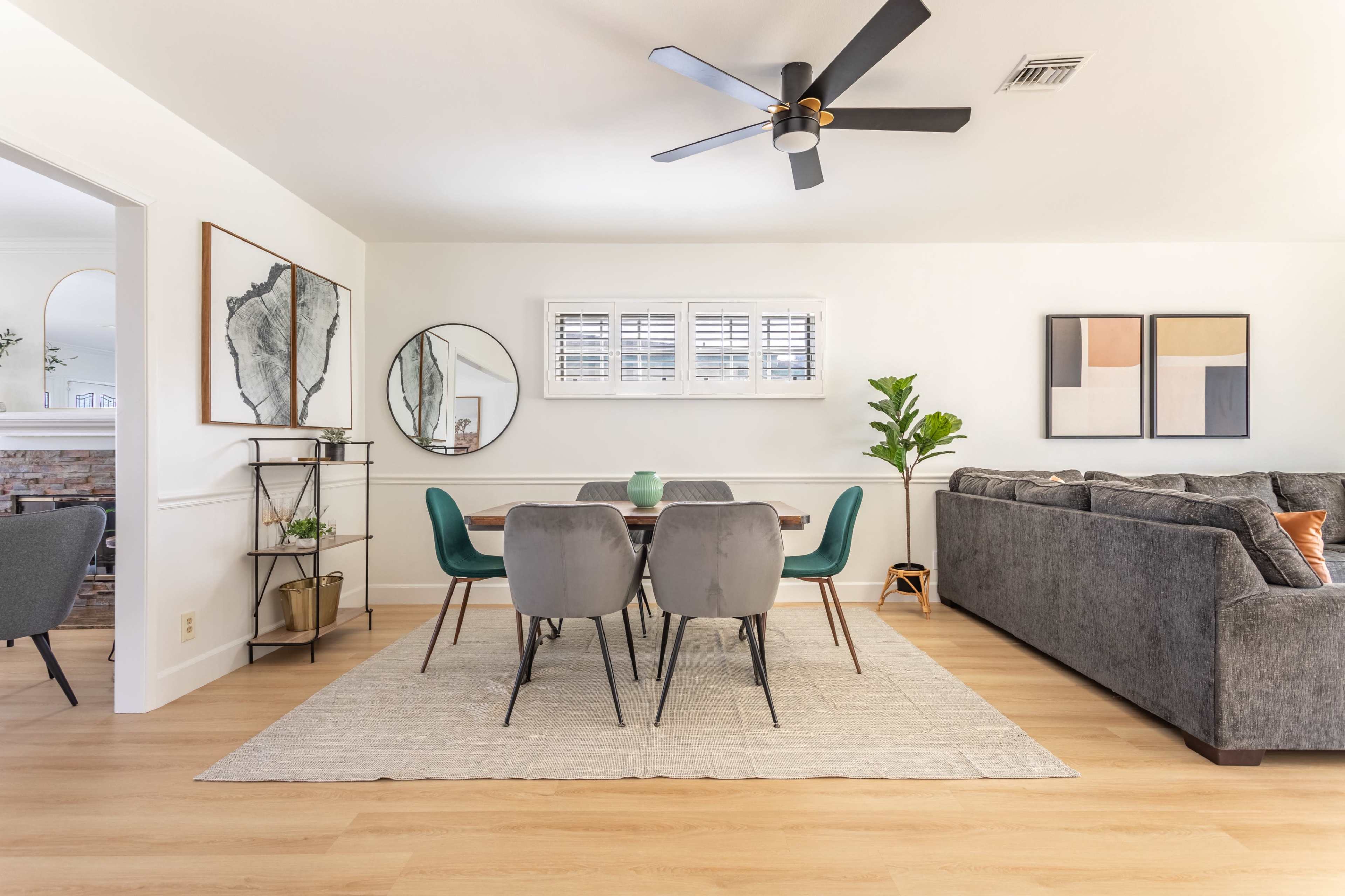 A modern living and dining area features a gray sofa, a rectangular dining table surrounded by chairs, and decorative elements like plants and artwork on the walls.