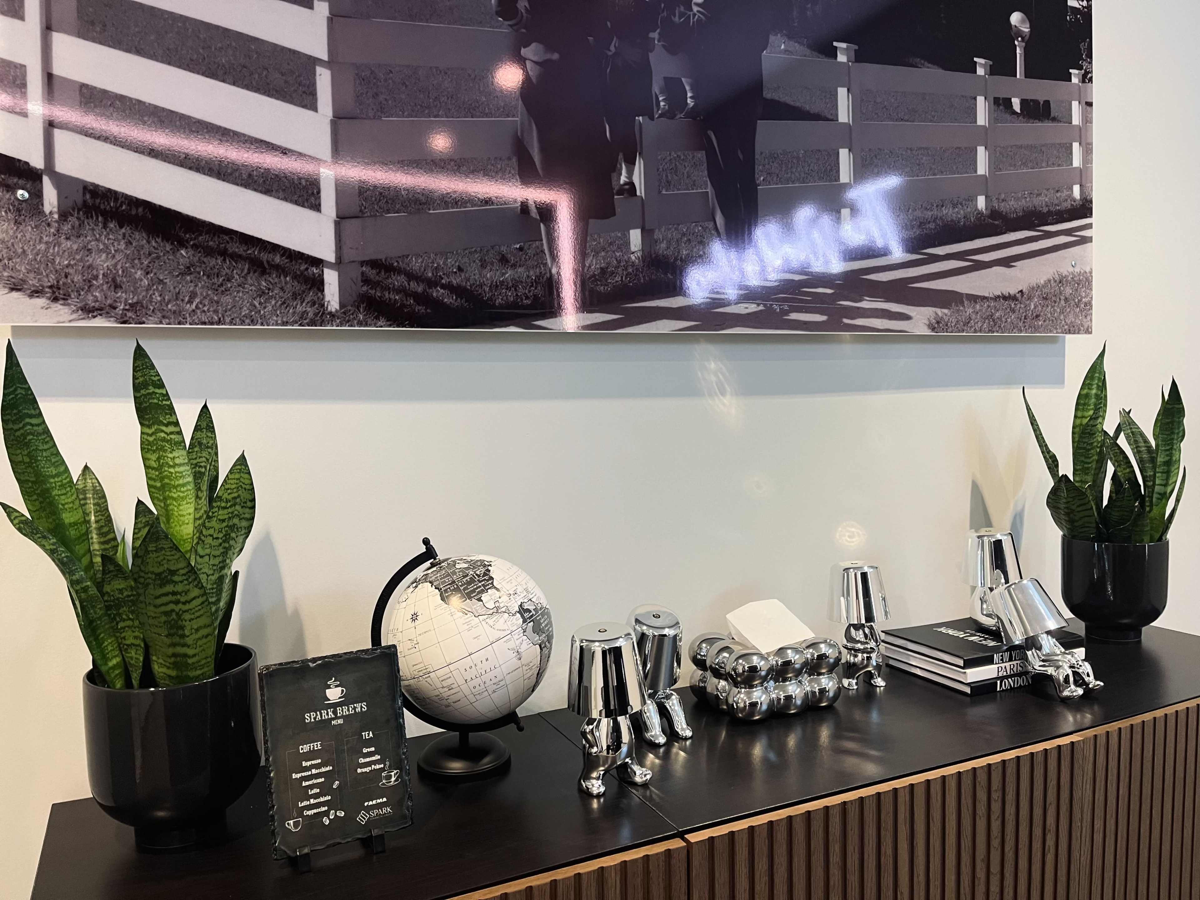 A wooden table displays a globe, various books, potted plants, and a menu on a stand beneath a large black-and-white photograph.