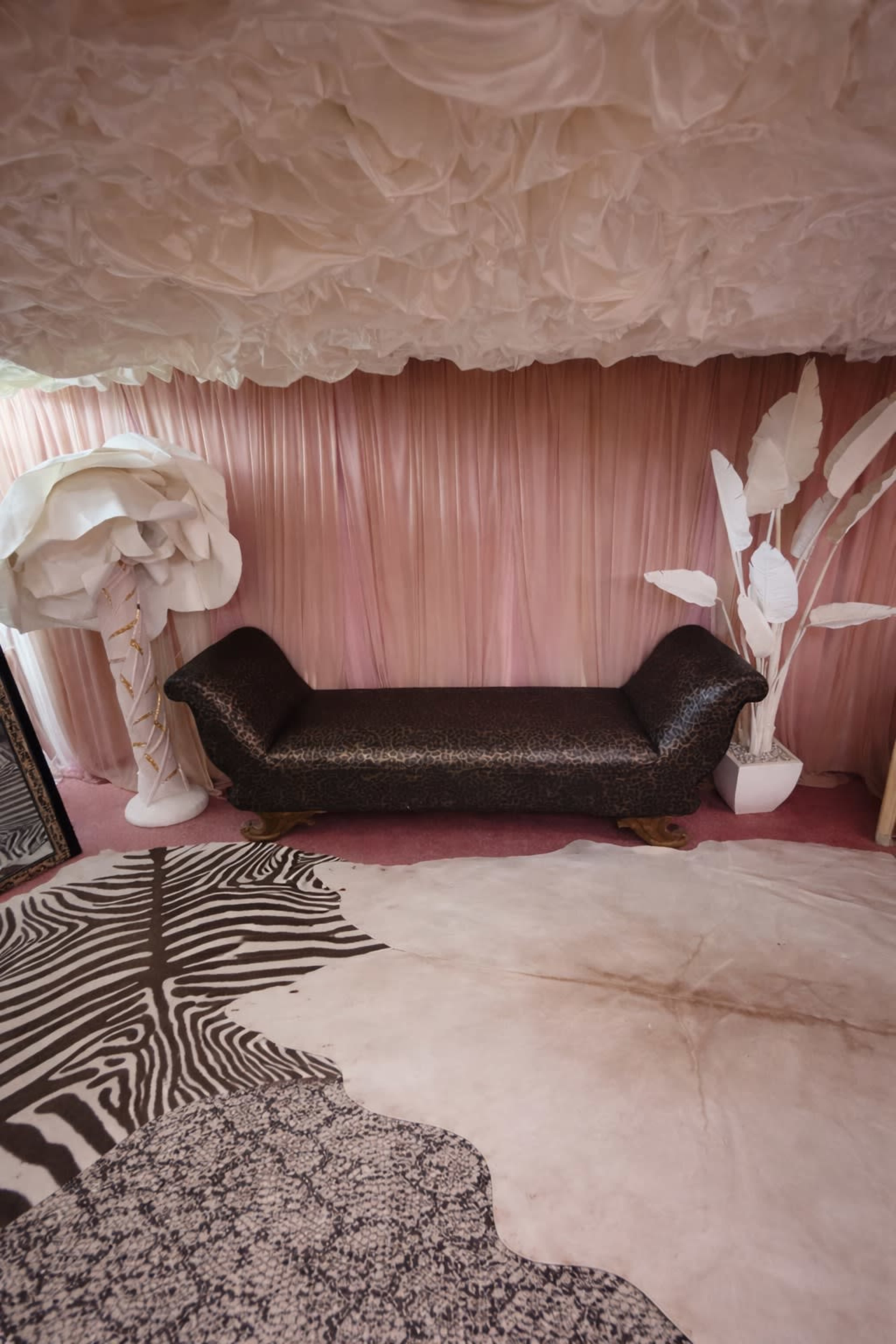 The image shows a stylized interior with a black couch, pink draped fabric on the walls, and cut-out white decorative elements resembling trees and plants.