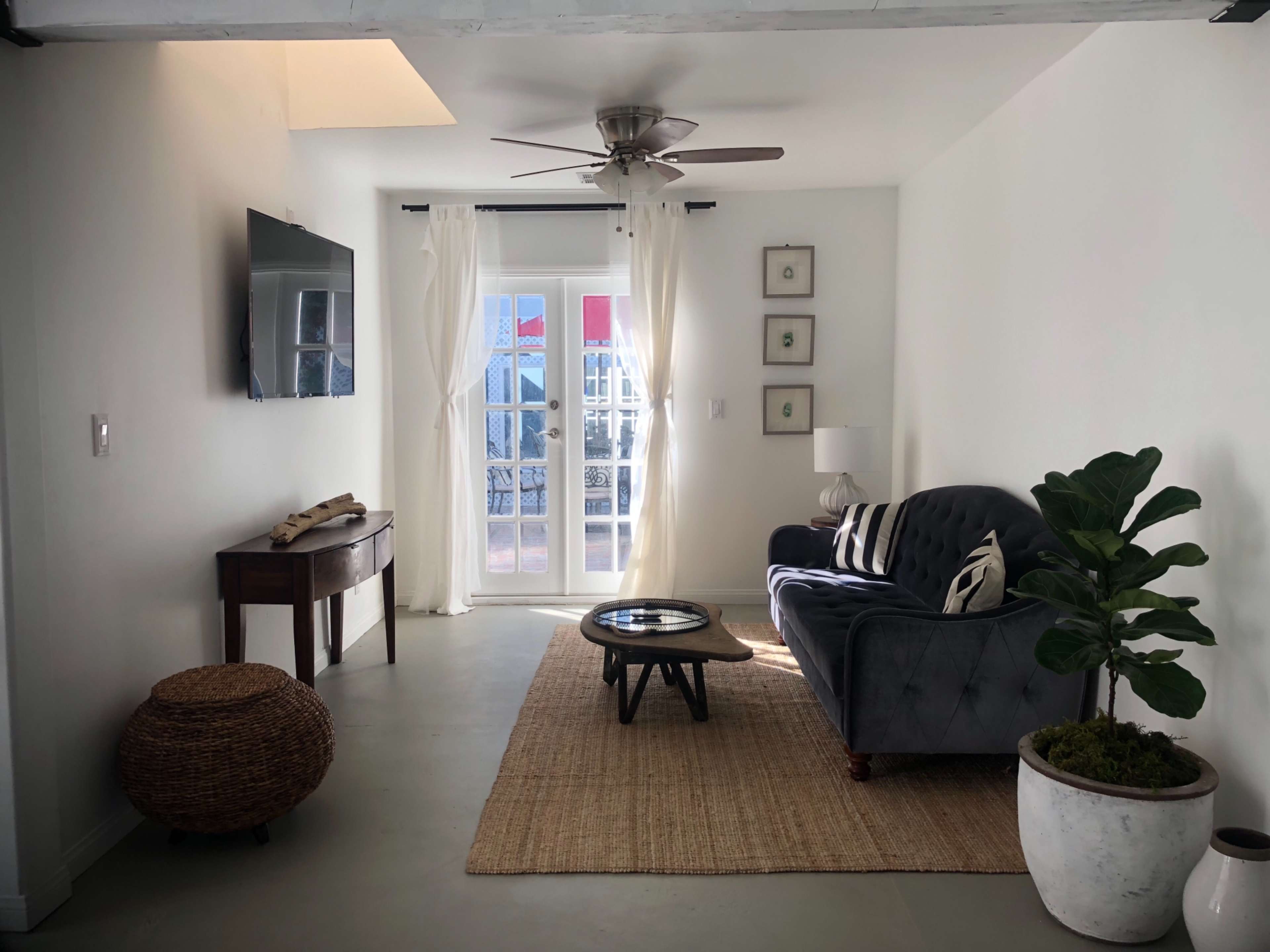 A modern living room features a gray couch, a round coffee table, and a decorative plant beside a window with sheer curtains.