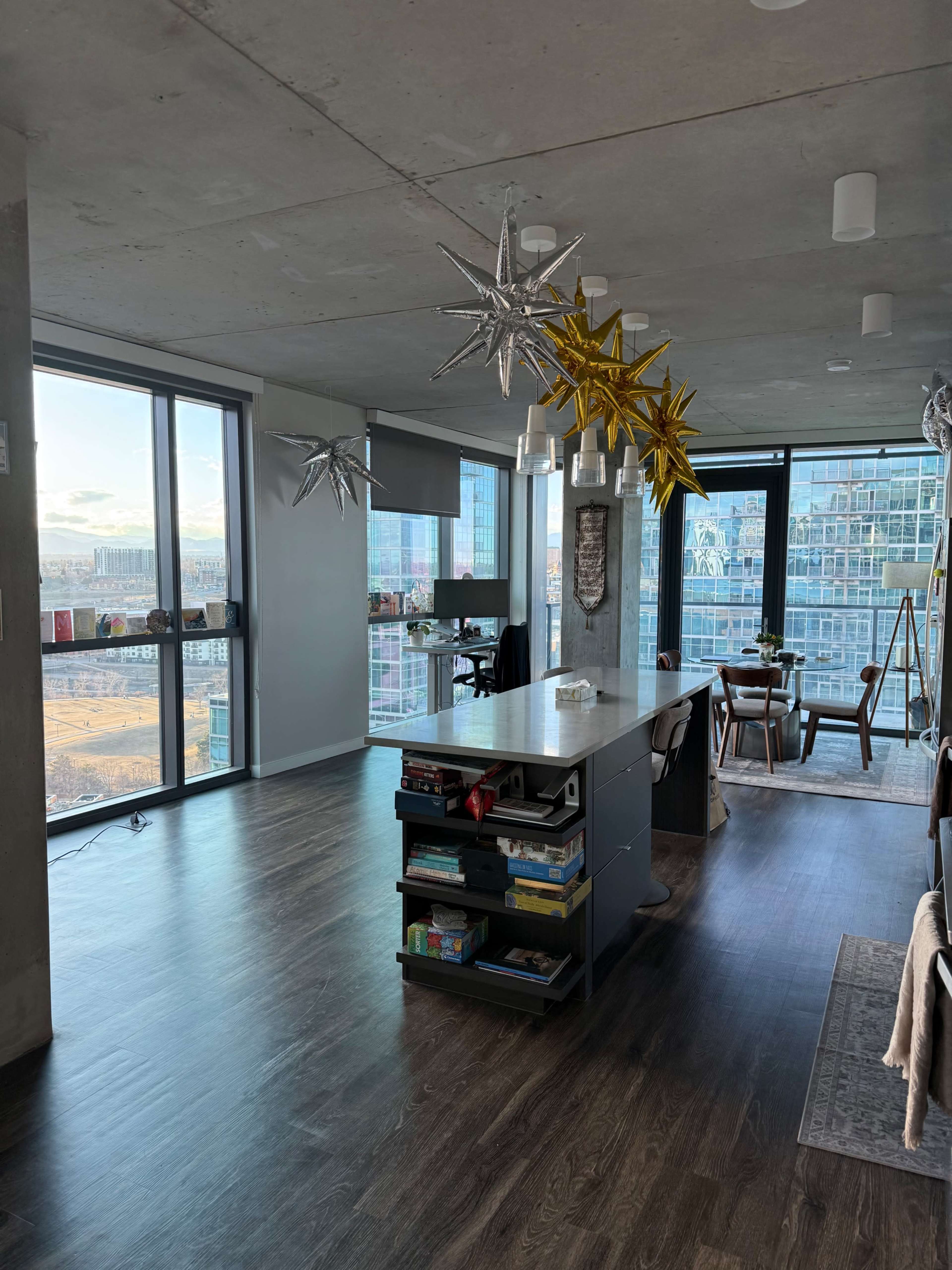 The image shows a modern apartment interior with large windows, a kitchen island, and decorative star-shaped light fixtures hanging from the ceiling.