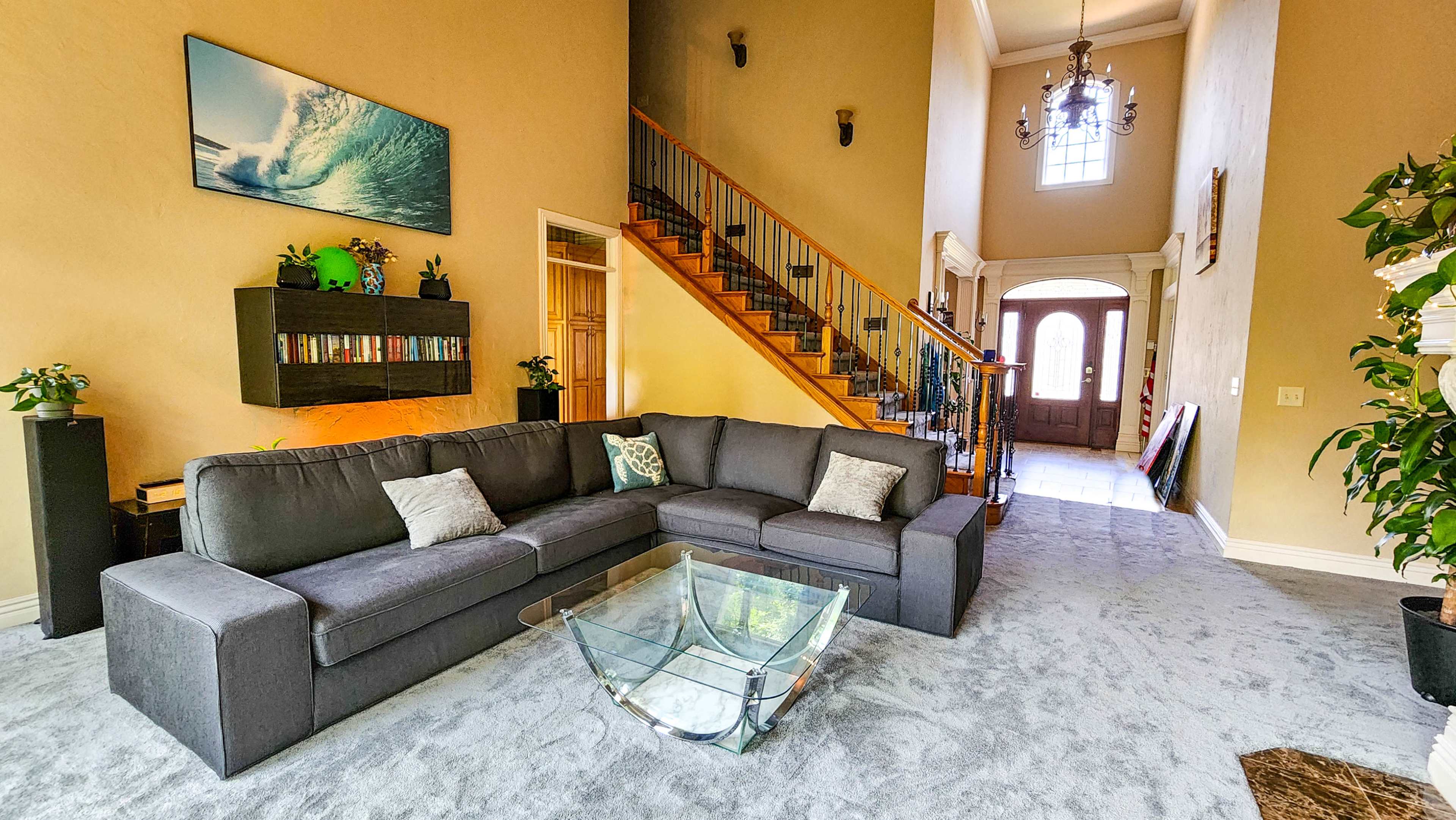 A spacious living room with a gray sectional sofa, a glass coffee table, and a staircase leading to an upper level.