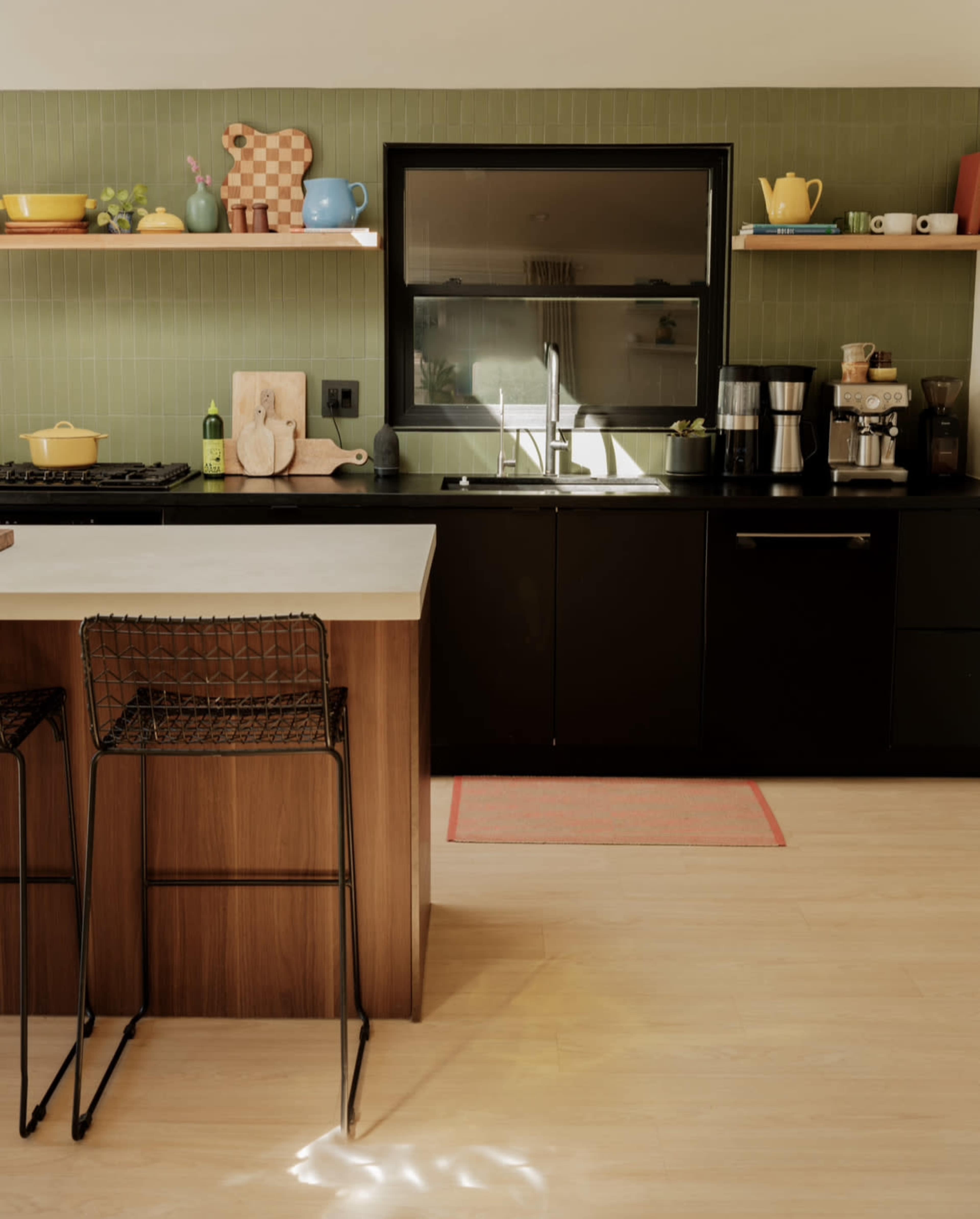 A modern kitchen features a black countertop, wooden bar stools, and a variety of colorful kitchenware displayed on shelves.
