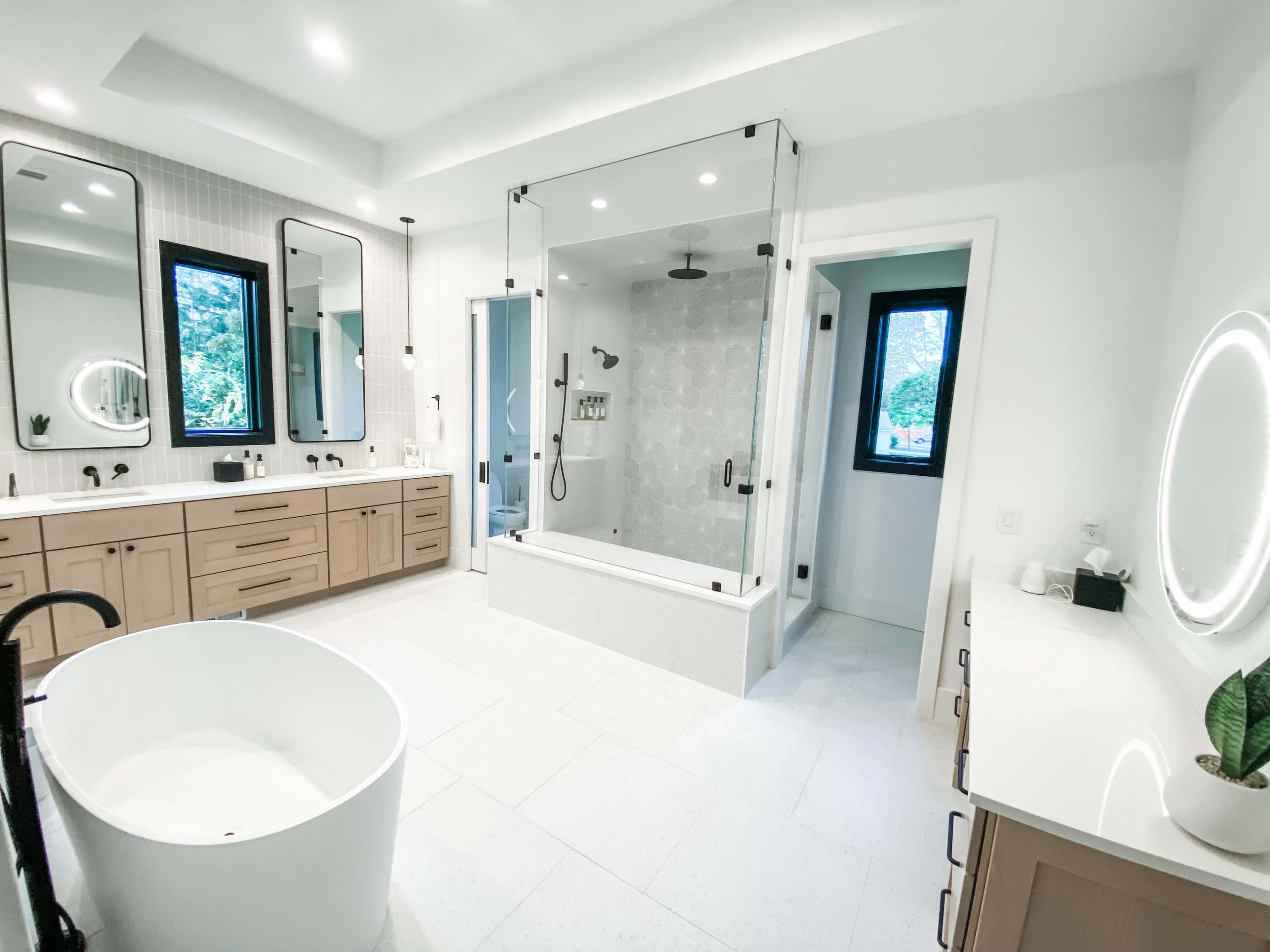 The bathroom features a spacious layout with a freestanding tub, double sinks, a glass-enclosed shower, and large mirrors with modern lighting.