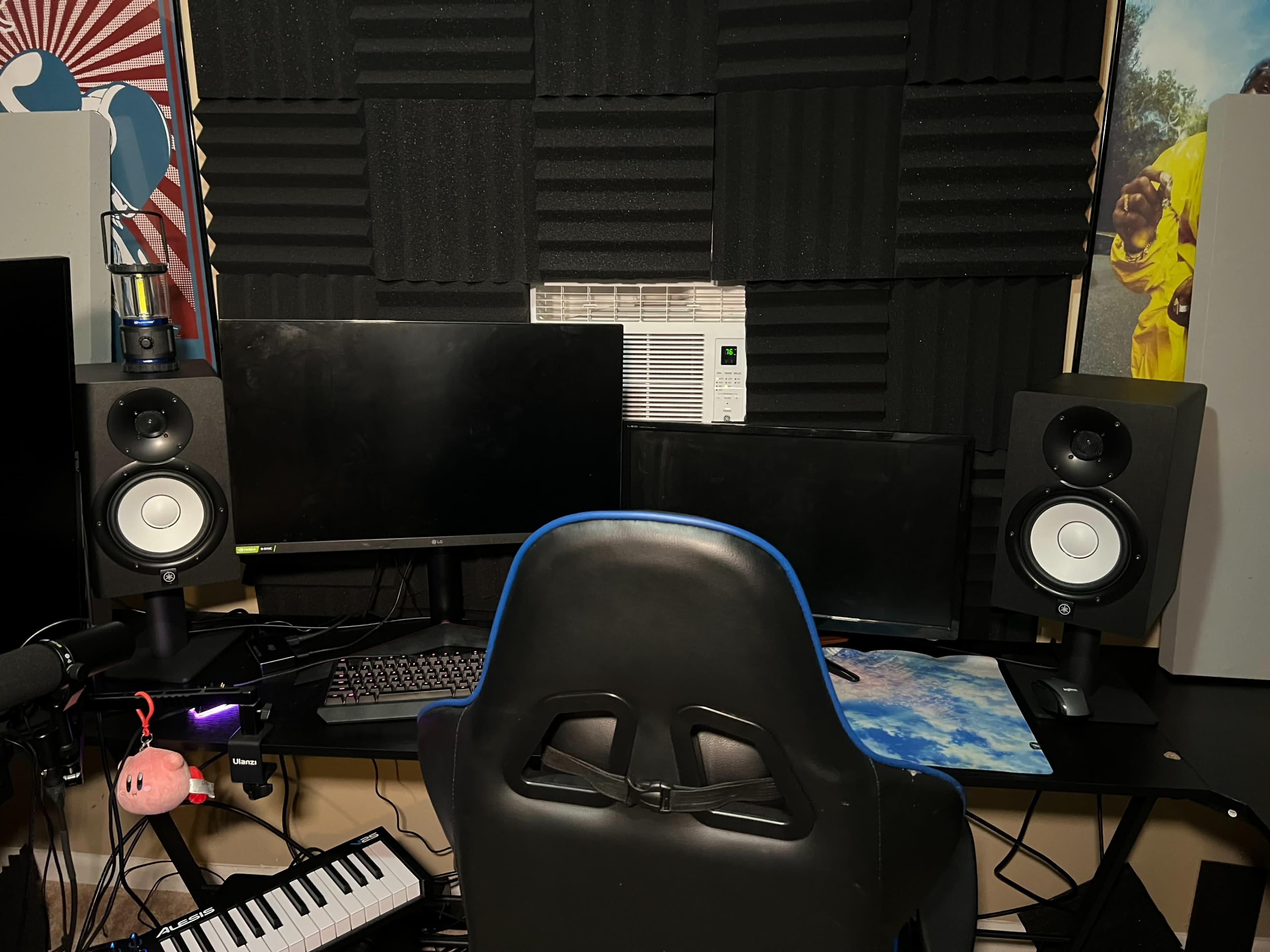 A home office setup featuring two computer monitors, speakers, a keyboard, and soundproofing foam on the walls.