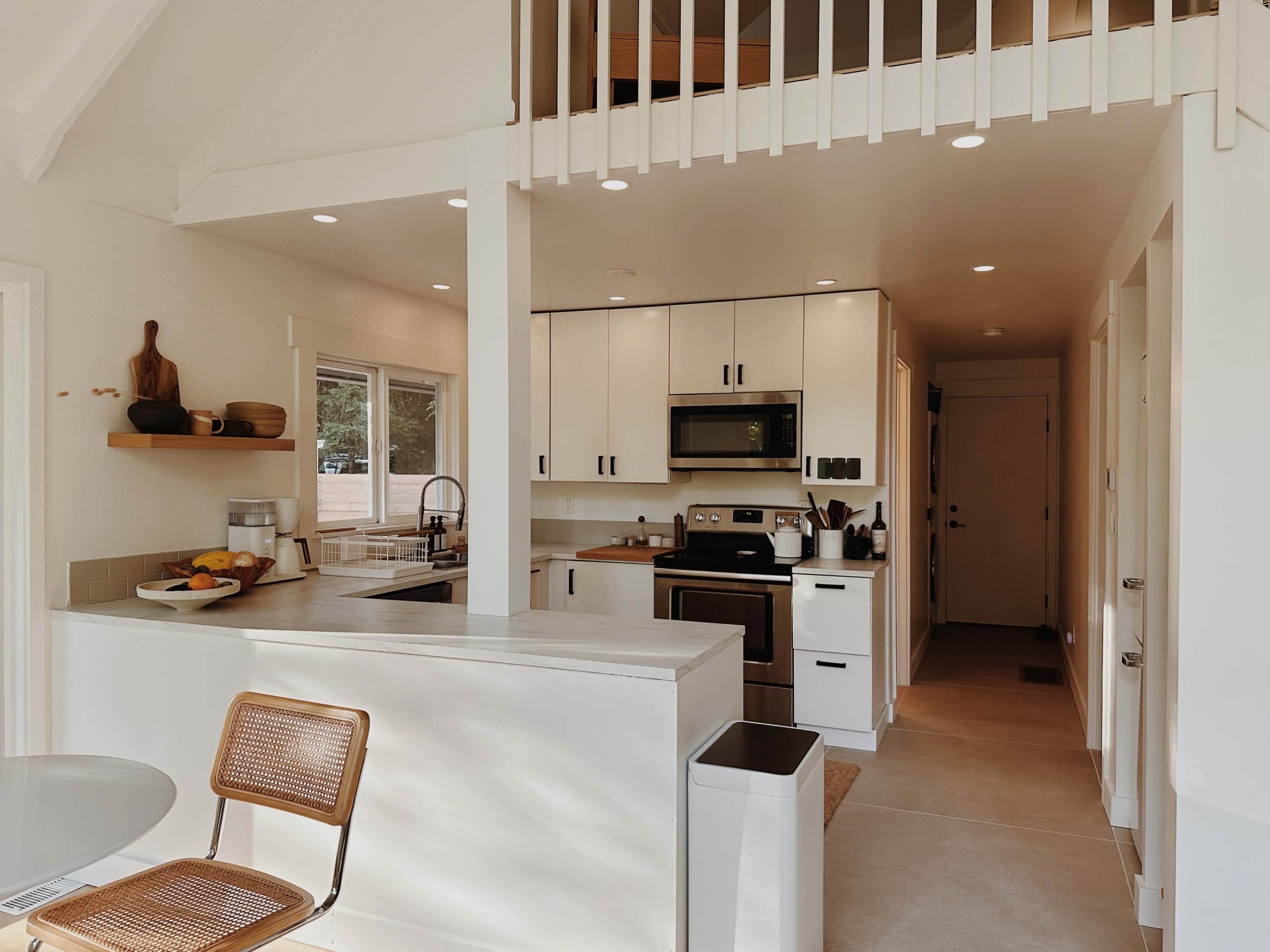 A modern kitchen and dining area with white cabinetry, stainless steel appliances, and a small table with a chair.