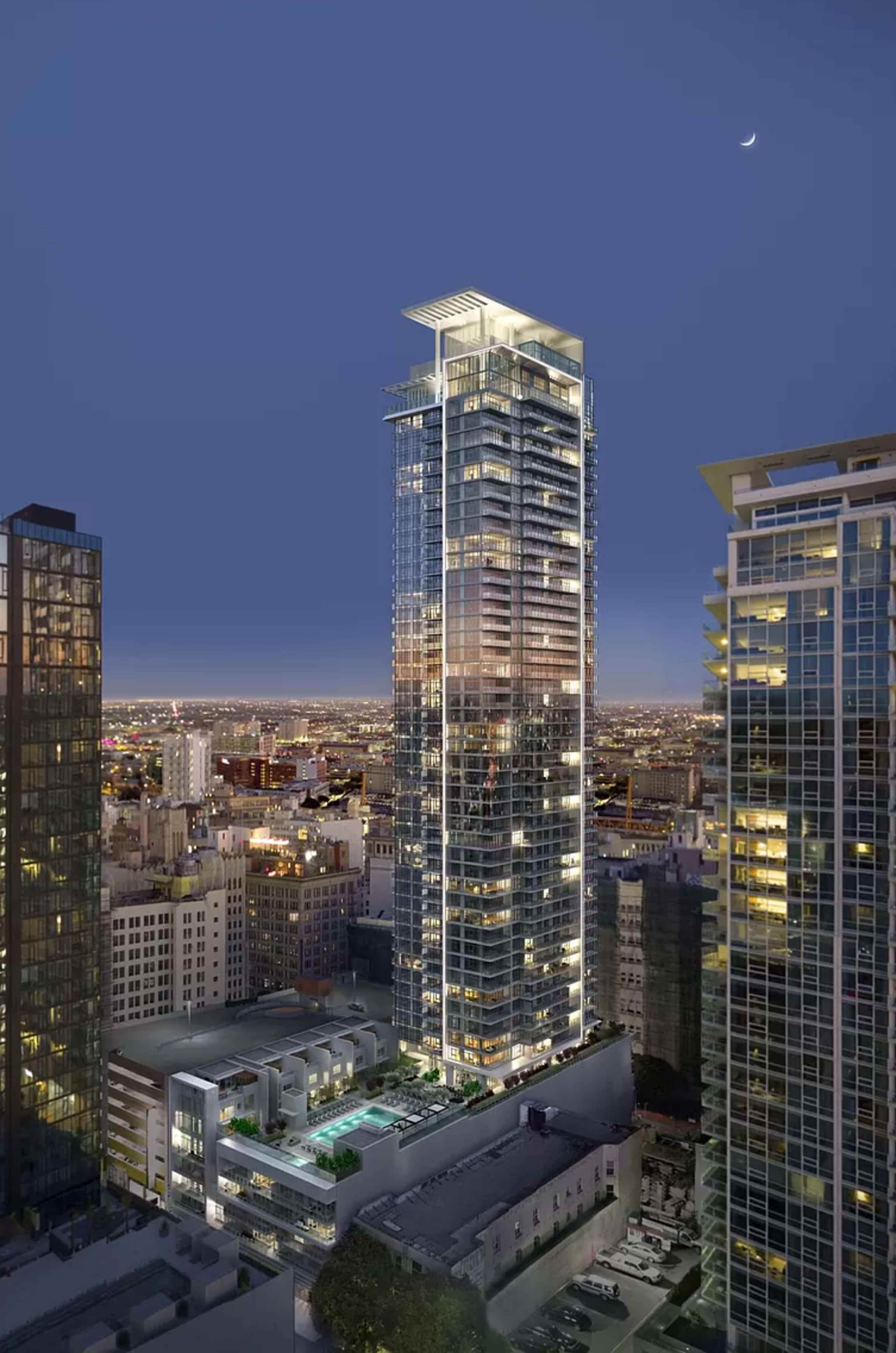 A tall, modern high-rise building with a glass facade is illuminated at night, surrounded by other skyscrapers in an urban setting.