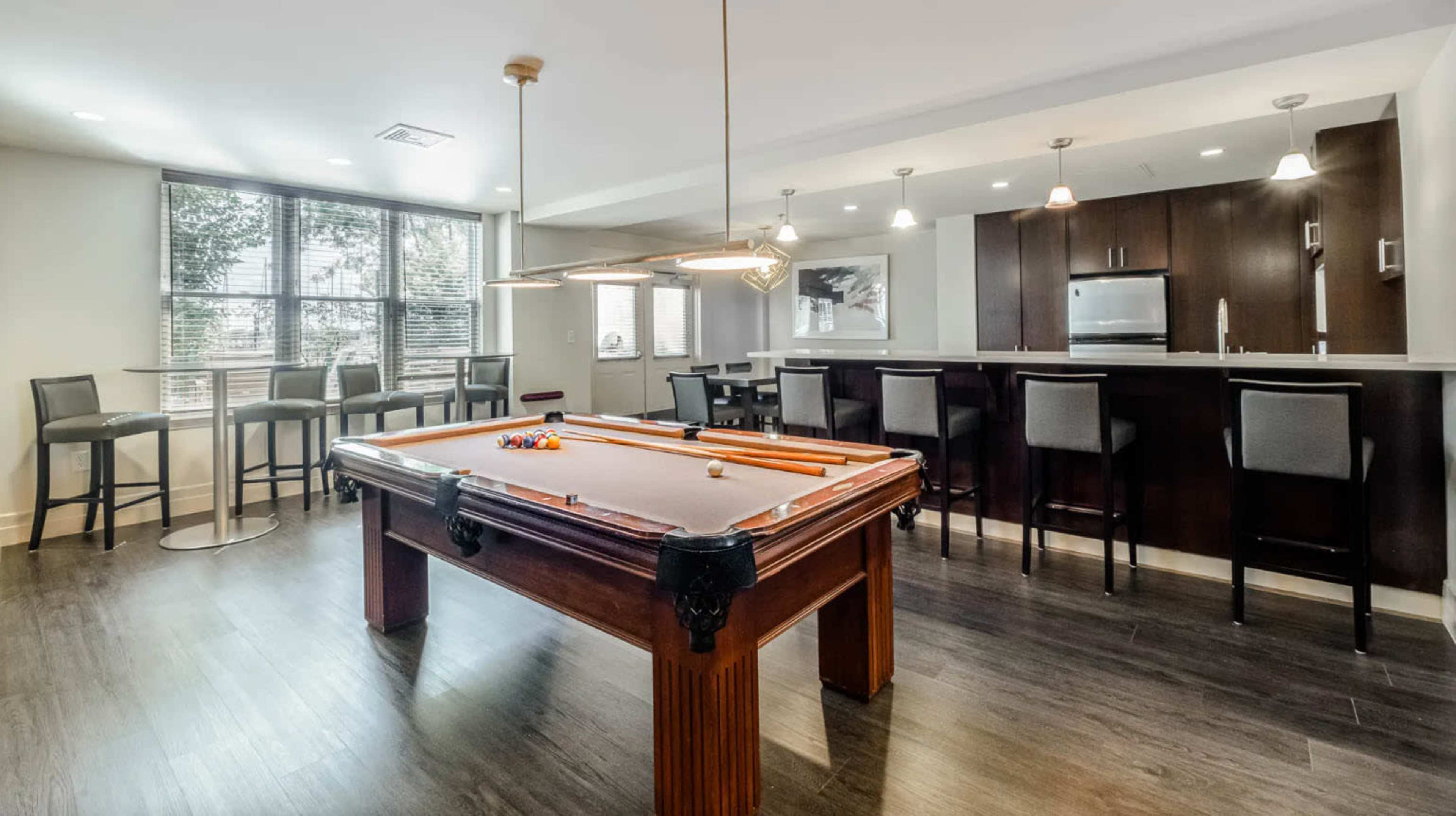 A modern room featuring a pool table in the center, surrounded by seating areas and a kitchenette in the background.