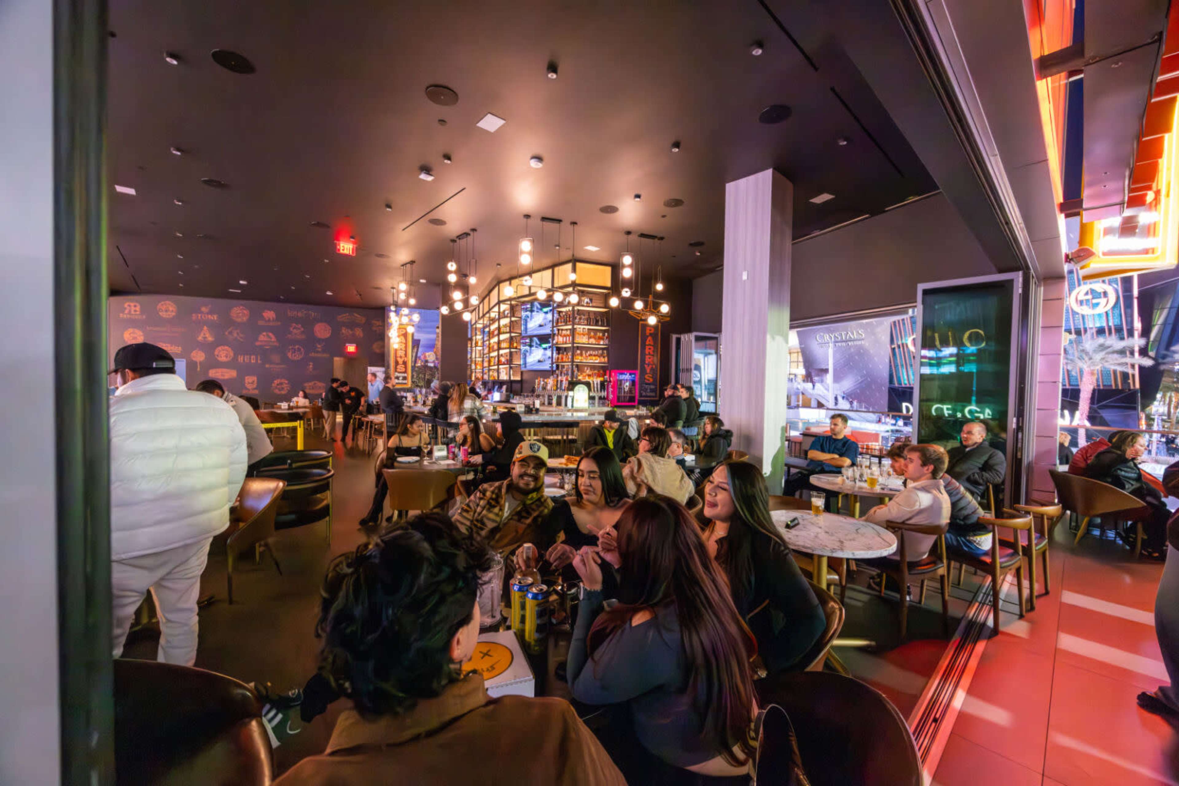 The image shows a bustling restaurant interior filled with people seated at tables, illuminated by ambient lighting and decorative fixtures.