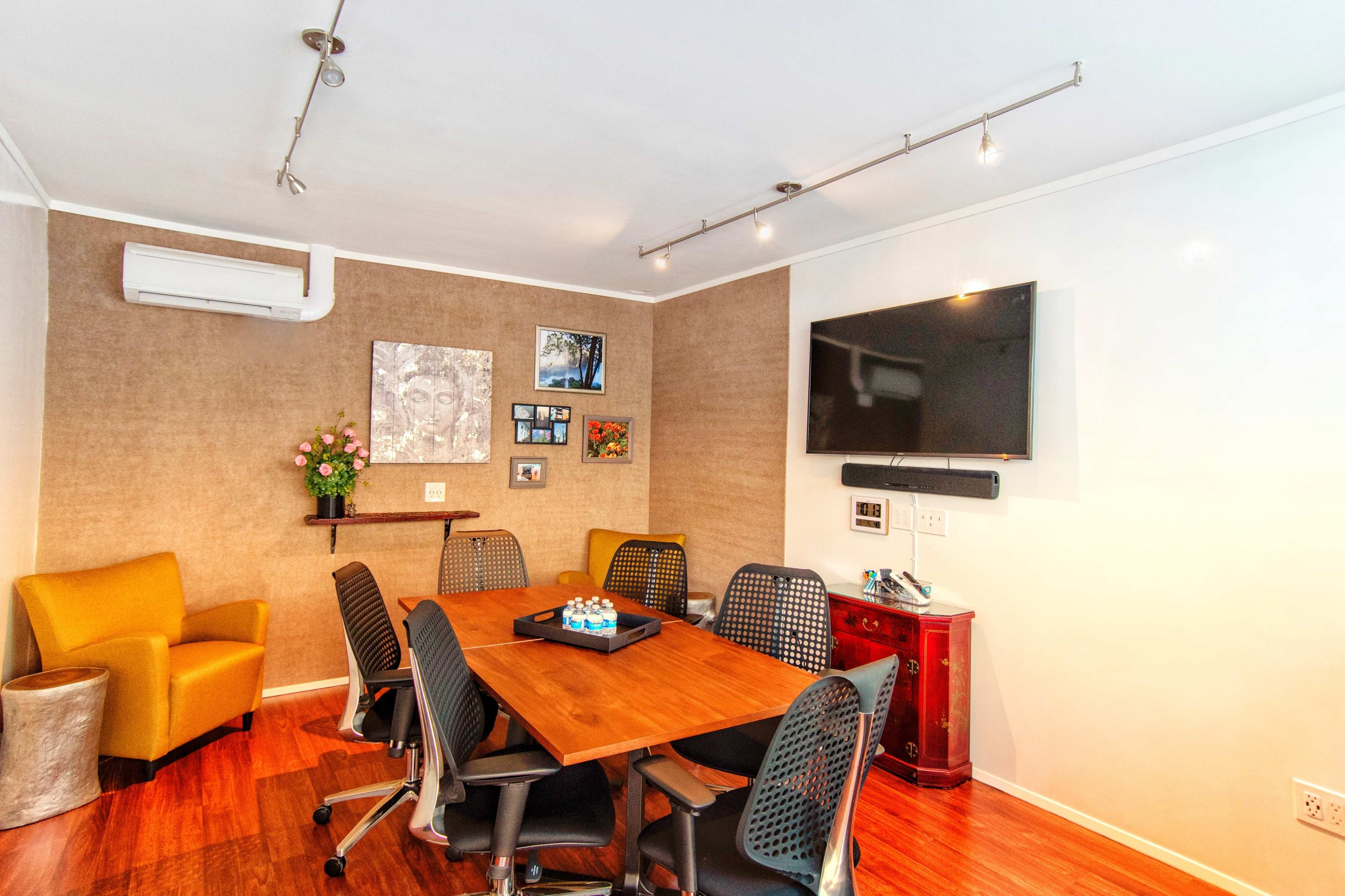 A conference room with a wooden table surrounded by chairs, a mounted TV, and decorative elements on the walls.