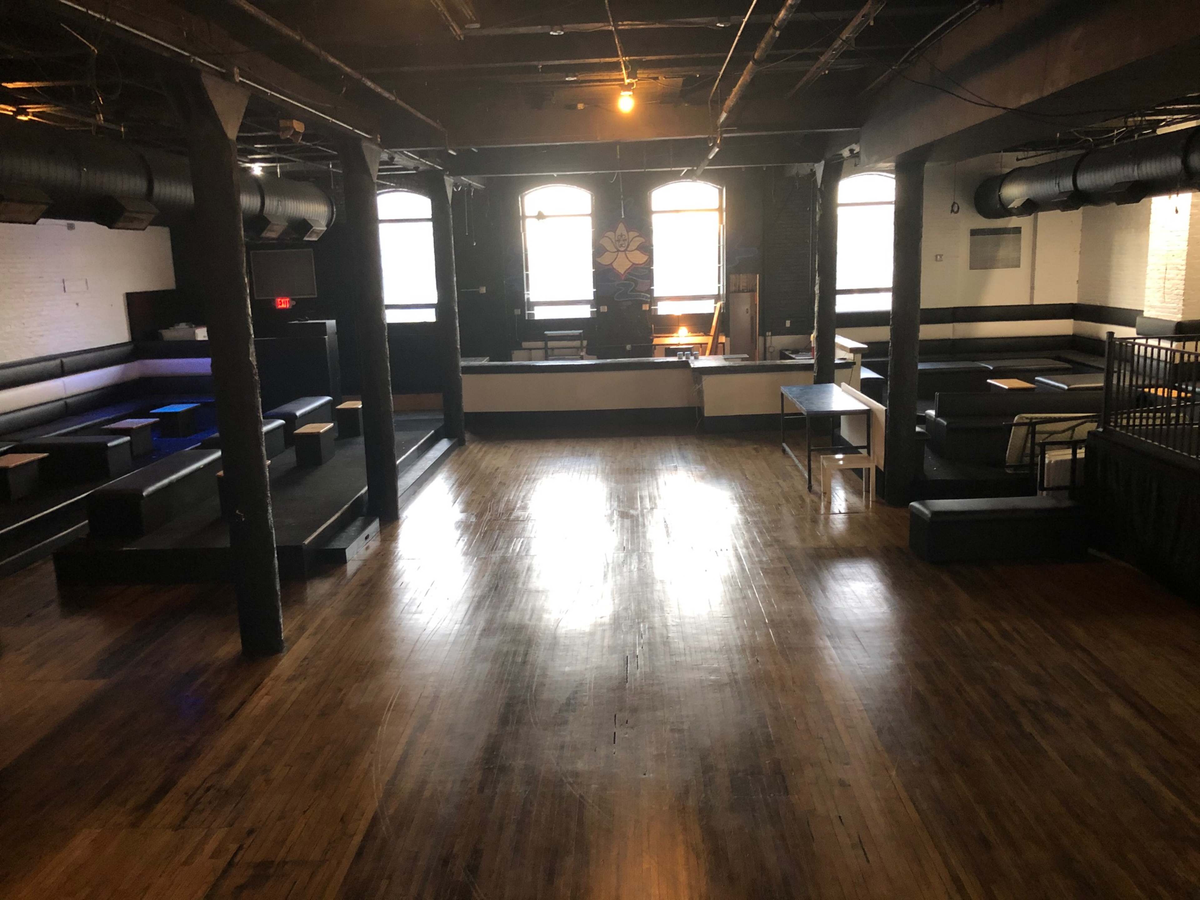 A spacious venue with wooden floors, multiple seating arrangements, and large windows allowing natural light.