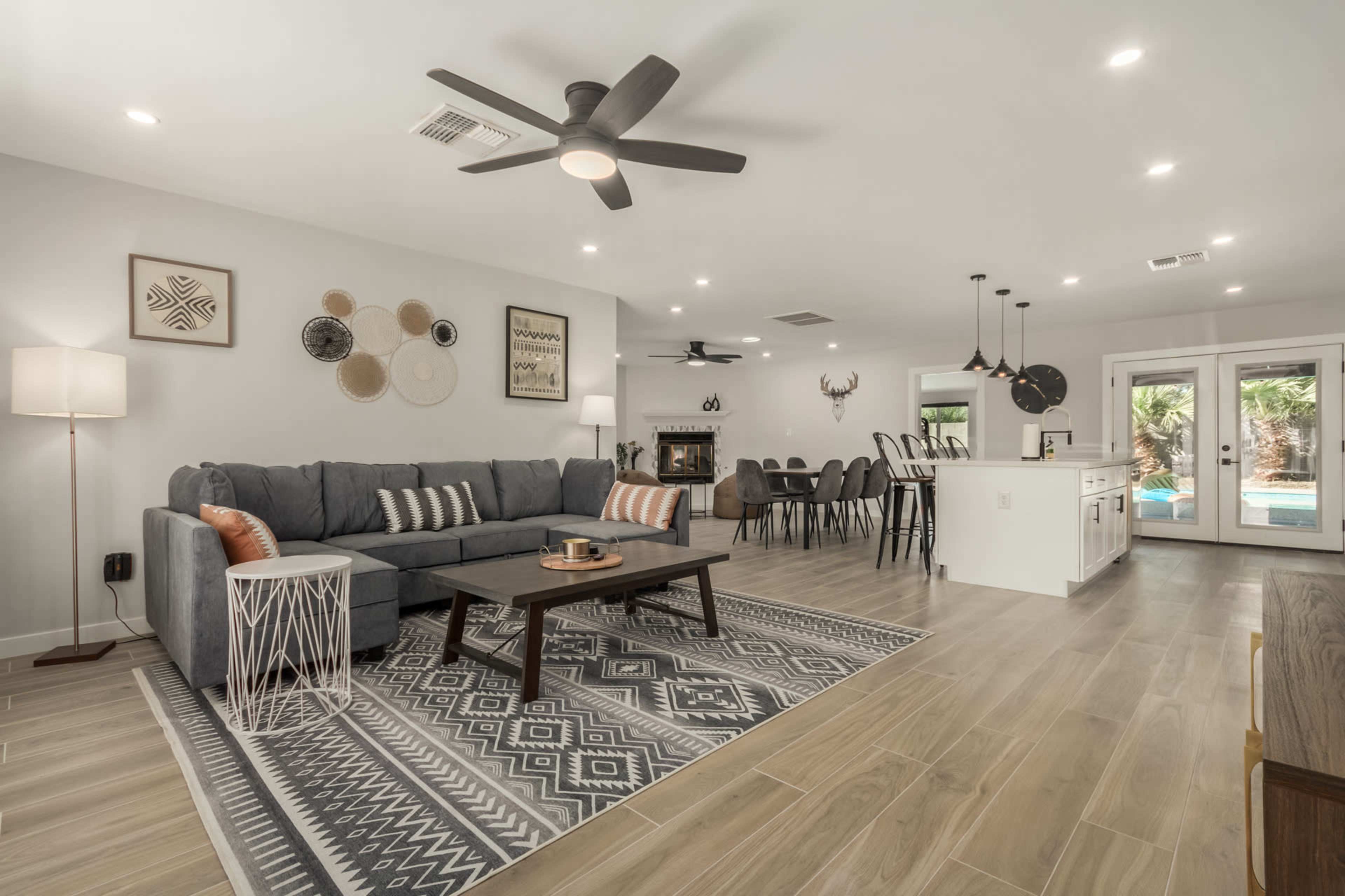 A modern living room featuring a gray sectional sofa, a geometric area rug, a coffee table, and a dining area that opens to a view of a pool.