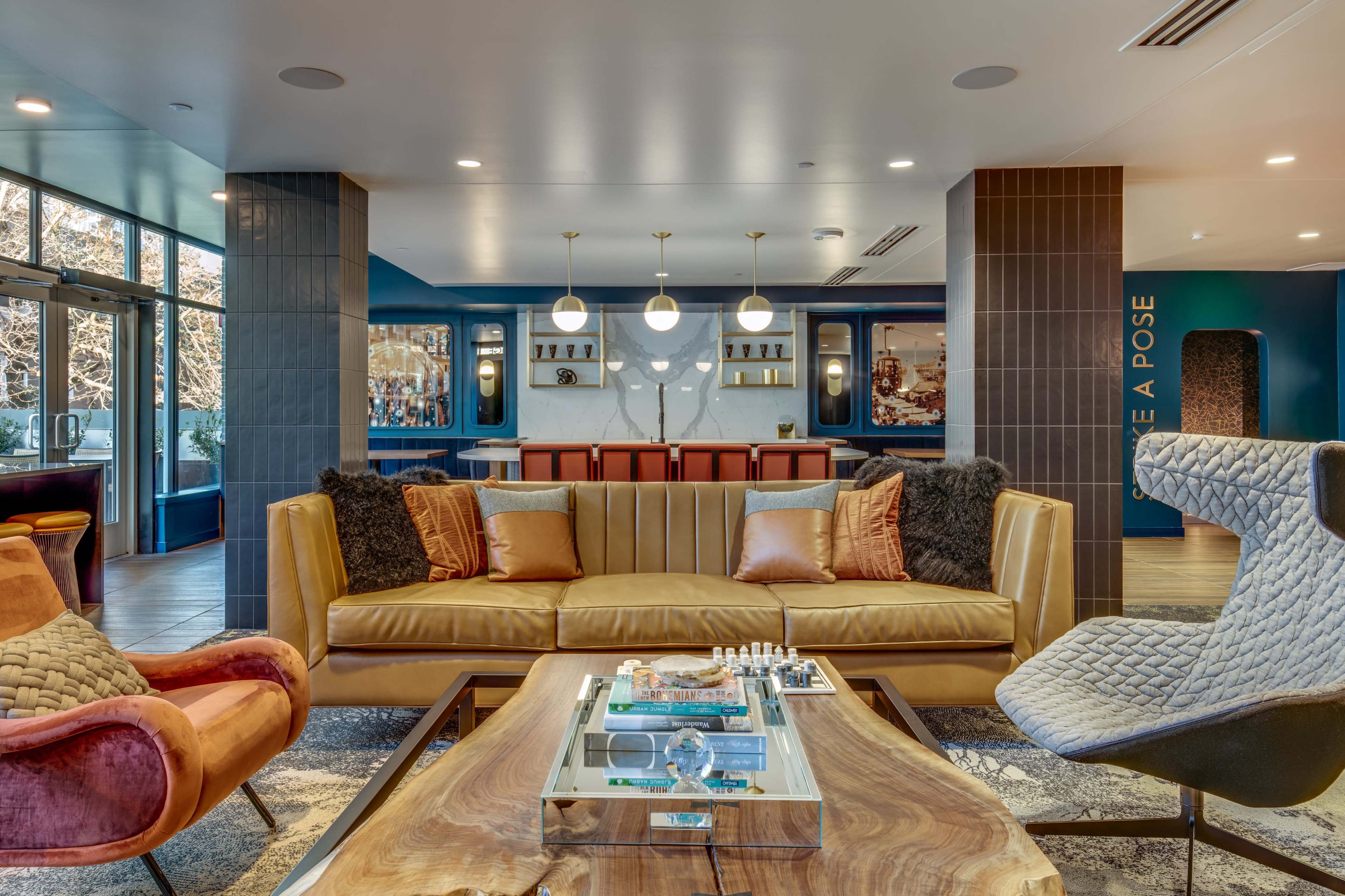 A modern lobby area featuring a yellow couch, two accent chairs, a coffee table with a chess set, and a bar in the background.