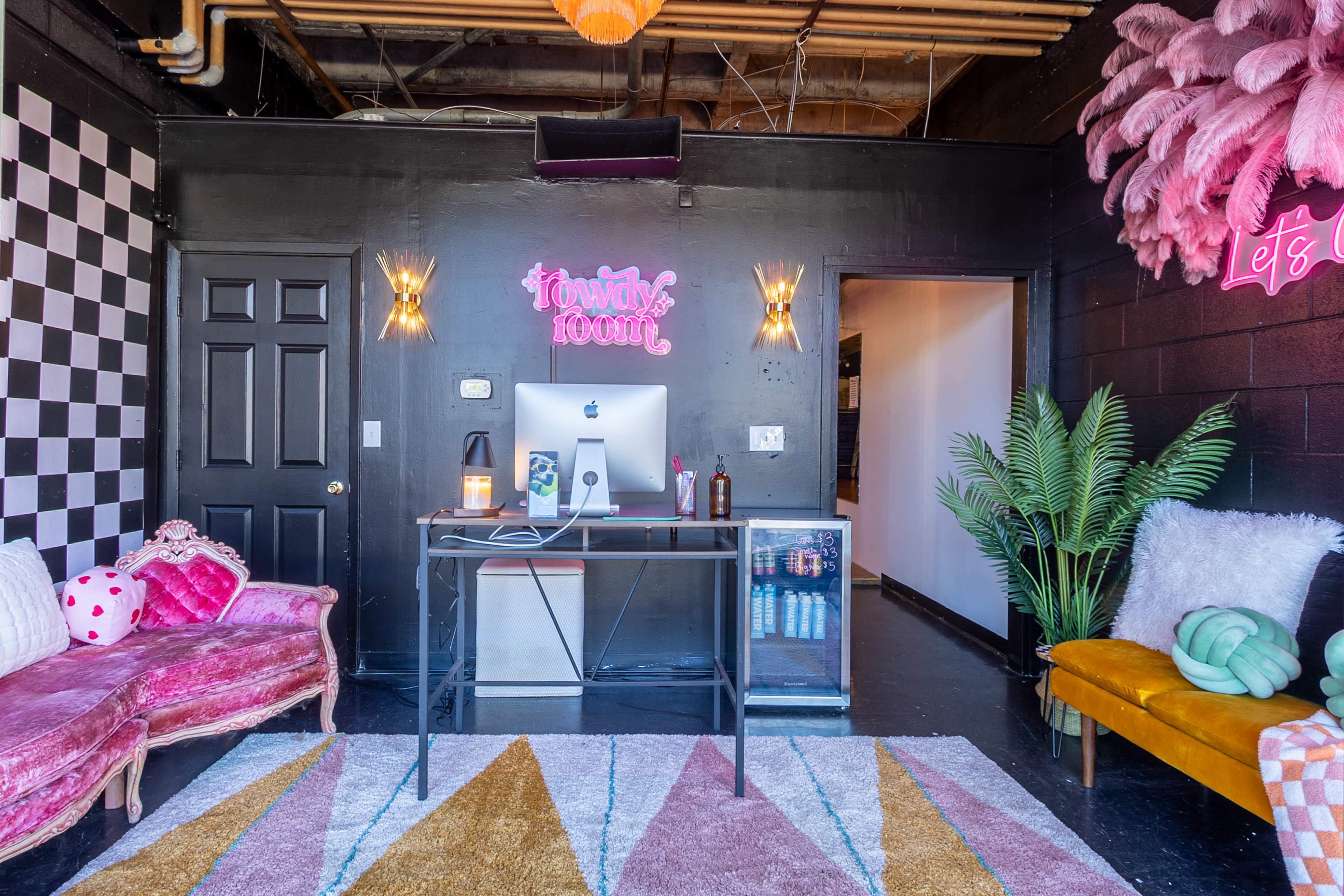 A stylish workspace featuring a desk with an iMac, colorful seating options, and decorative elements on black walls.