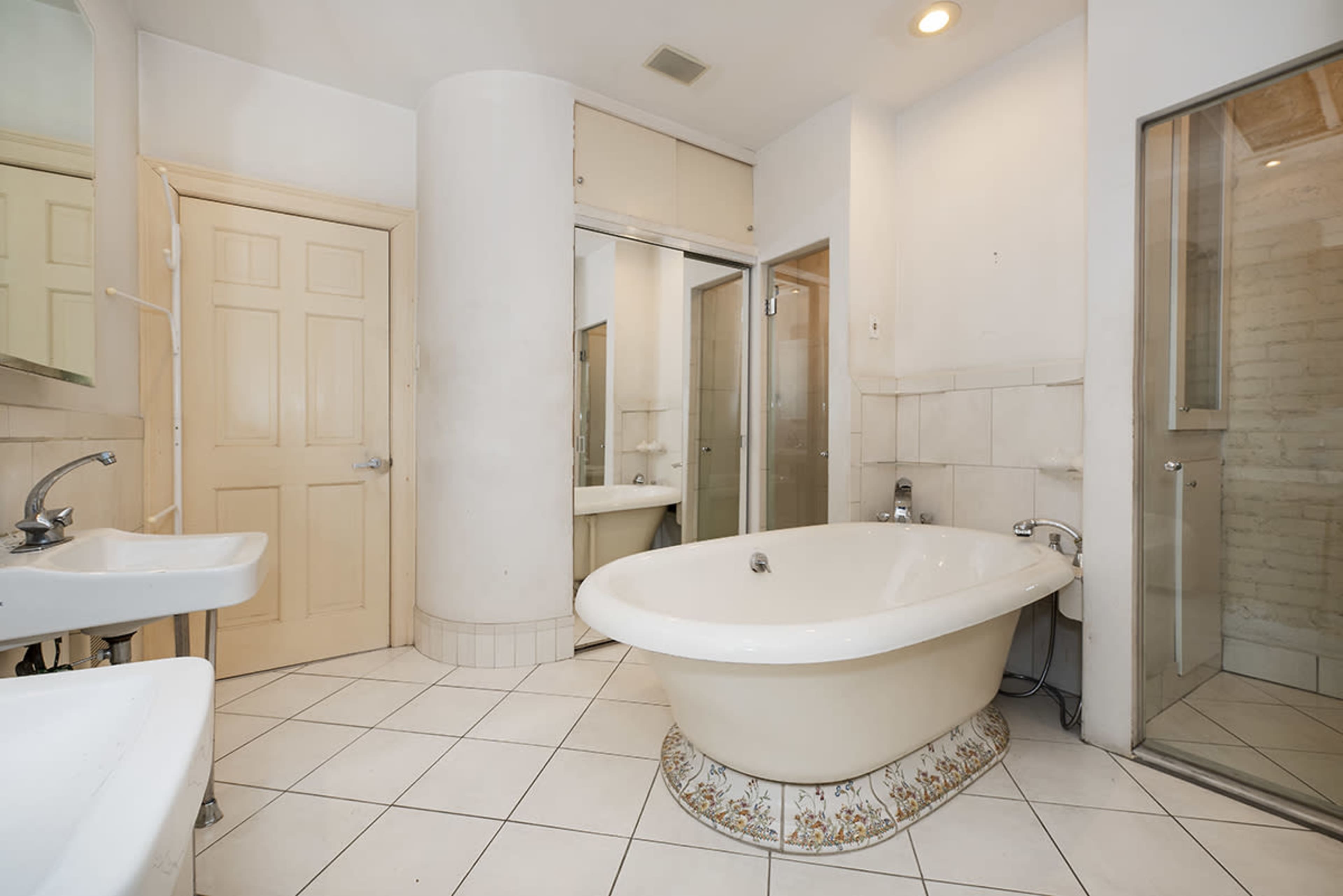 A bathroom features a freestanding bathtub, a glass shower enclosure, and dual sinks, all surrounded by tiled walls and floors.