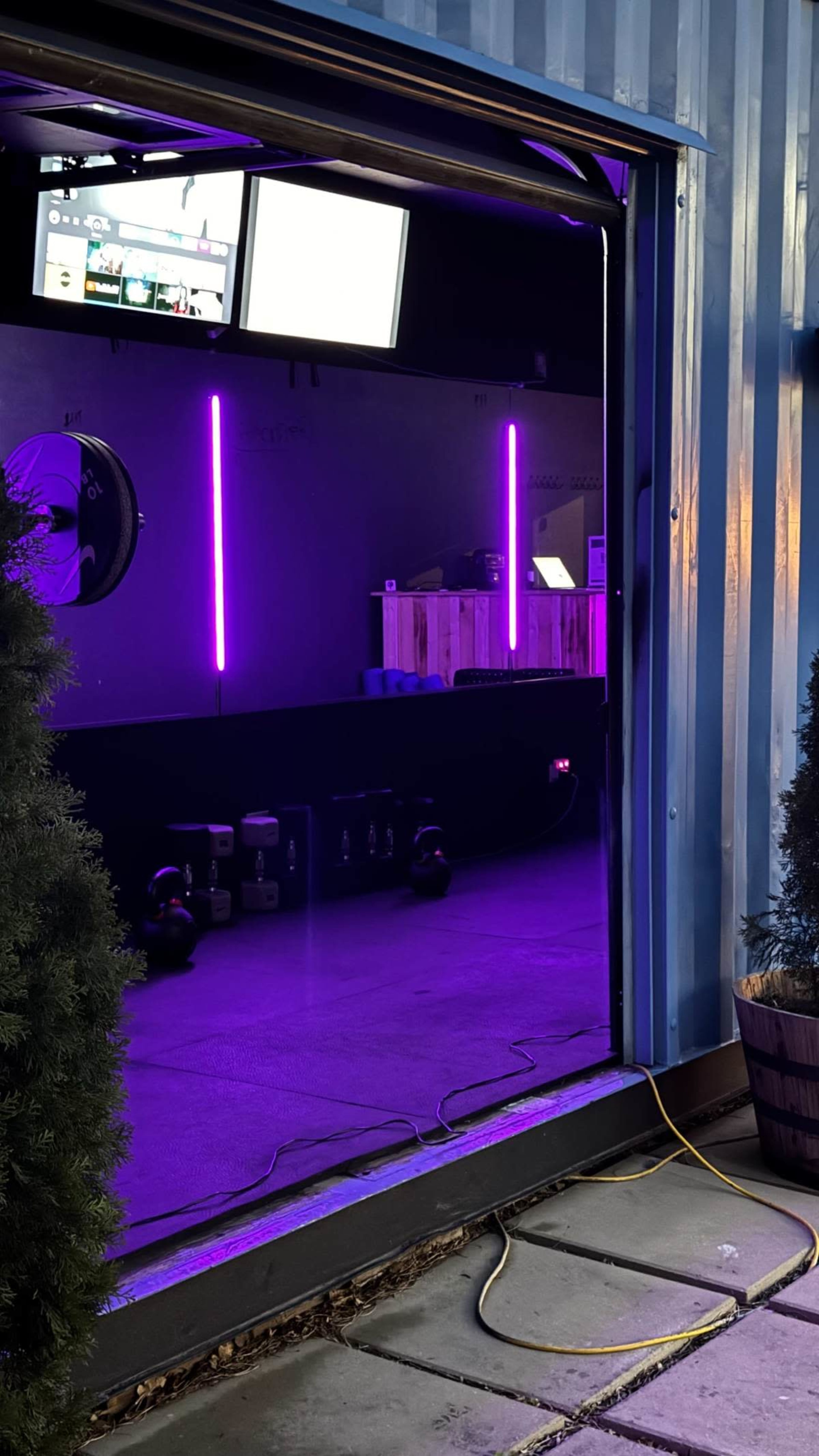 The image shows a gym space with purple LED lights, visible exercise equipment, and two screens mounted on the wall.