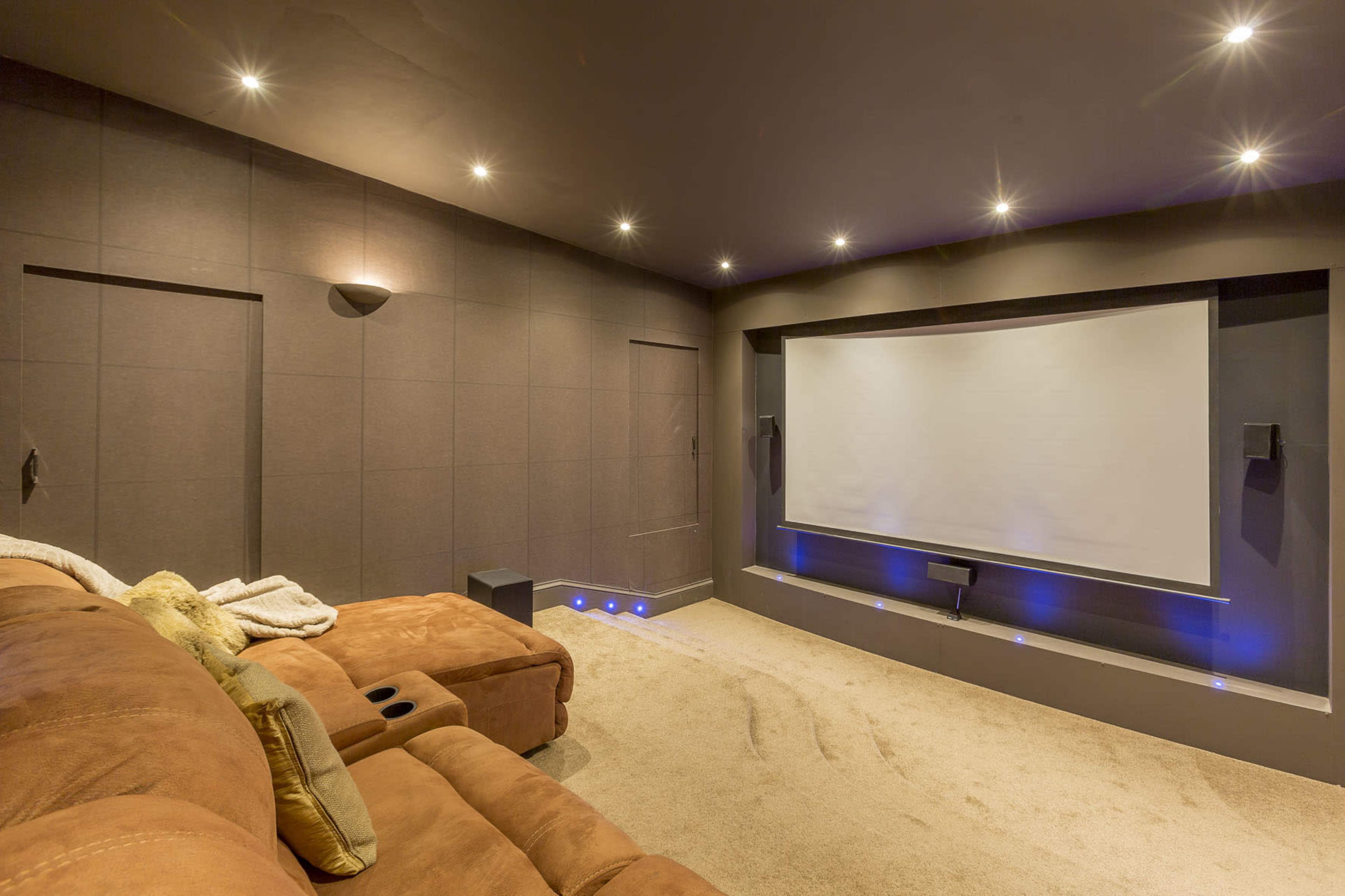 A home theater room features a large projection screen, dark walls, and a brown sectional sofa.